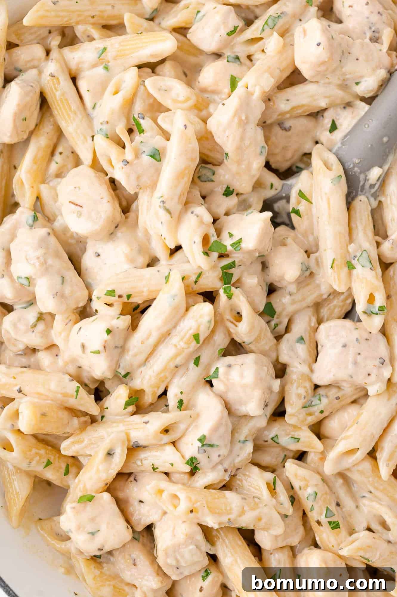 Creamy Chicken Skillet Pasta 2 A close-up of creamy penne pasta mixed with perfectly diced chicken and garnished with vibrant chopped fresh herbs, showcasing the rich texture and appealing presentation of this one-pan dish.