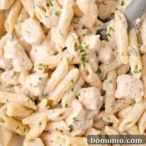 Close-up of creamy pasta with penne, tender chunks of chicken, and a fresh parsley garnish, ready to be served.