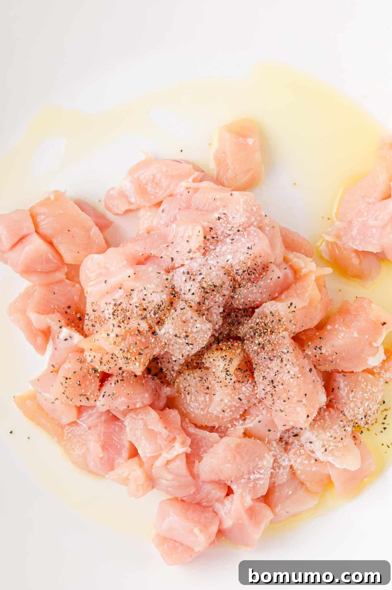 Creamy Chicken Skillet Pasta 5 Diced raw chicken seasoned with salt, pepper, and olive oil, glistening on a white surface, prepared for searing and ready for the hot pan.