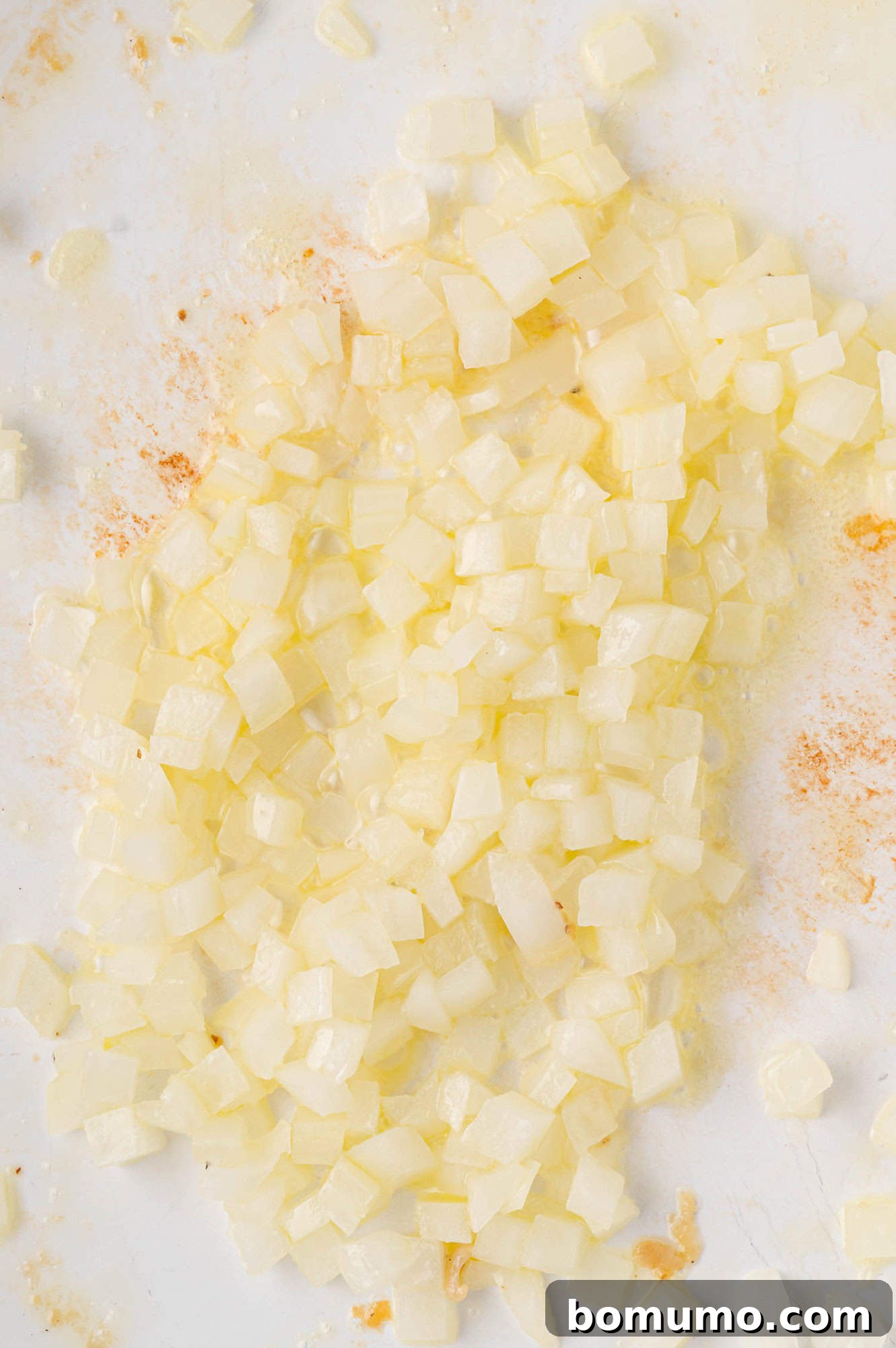 Creamy Chicken Skillet Pasta 7 Finely diced onions gently sizzling in a white pan with a subtle sheen of olive oil, showing minimal seasoning, slowly softening to release their flavor.