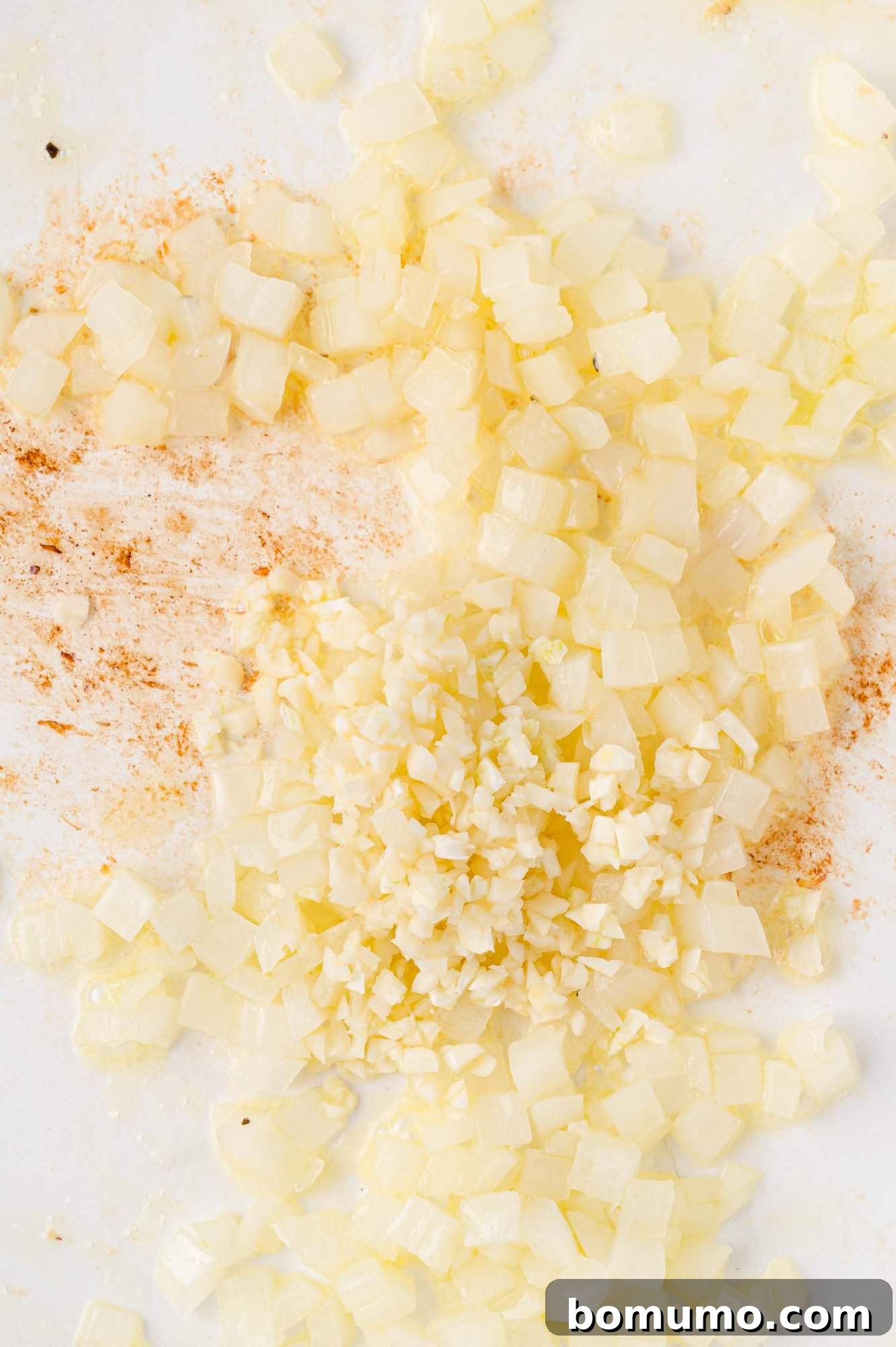 Creamy Chicken Skillet Pasta 8 Aromatic combination of finely chopped garlic and diced onions, perfectly sautéed in a white pan, enhanced with a light sprinkle of ground spices, releasing inviting aromas.