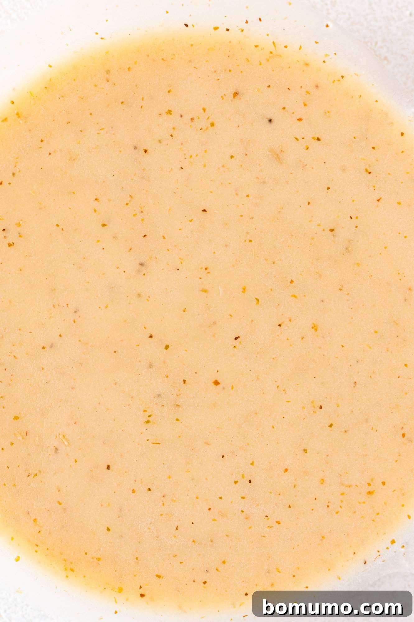 Creamy beige salad dressing with visible specks of spices, filling the frame.