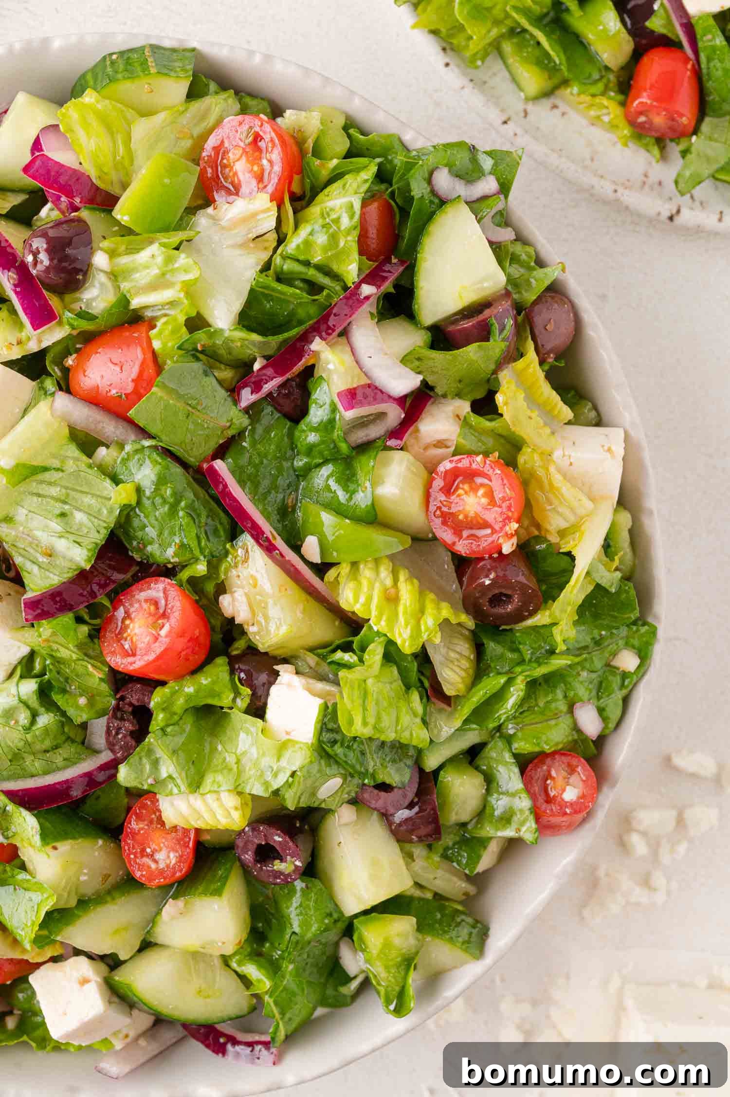 A vibrant bowl of modernized Greek salad, featuring crisp romaine lettuce, bright cherry tomatoes, cool cucumber, thinly sliced red onion, briny Kalamata olives, and generous cubes of feta cheese, all perfectly dressed.