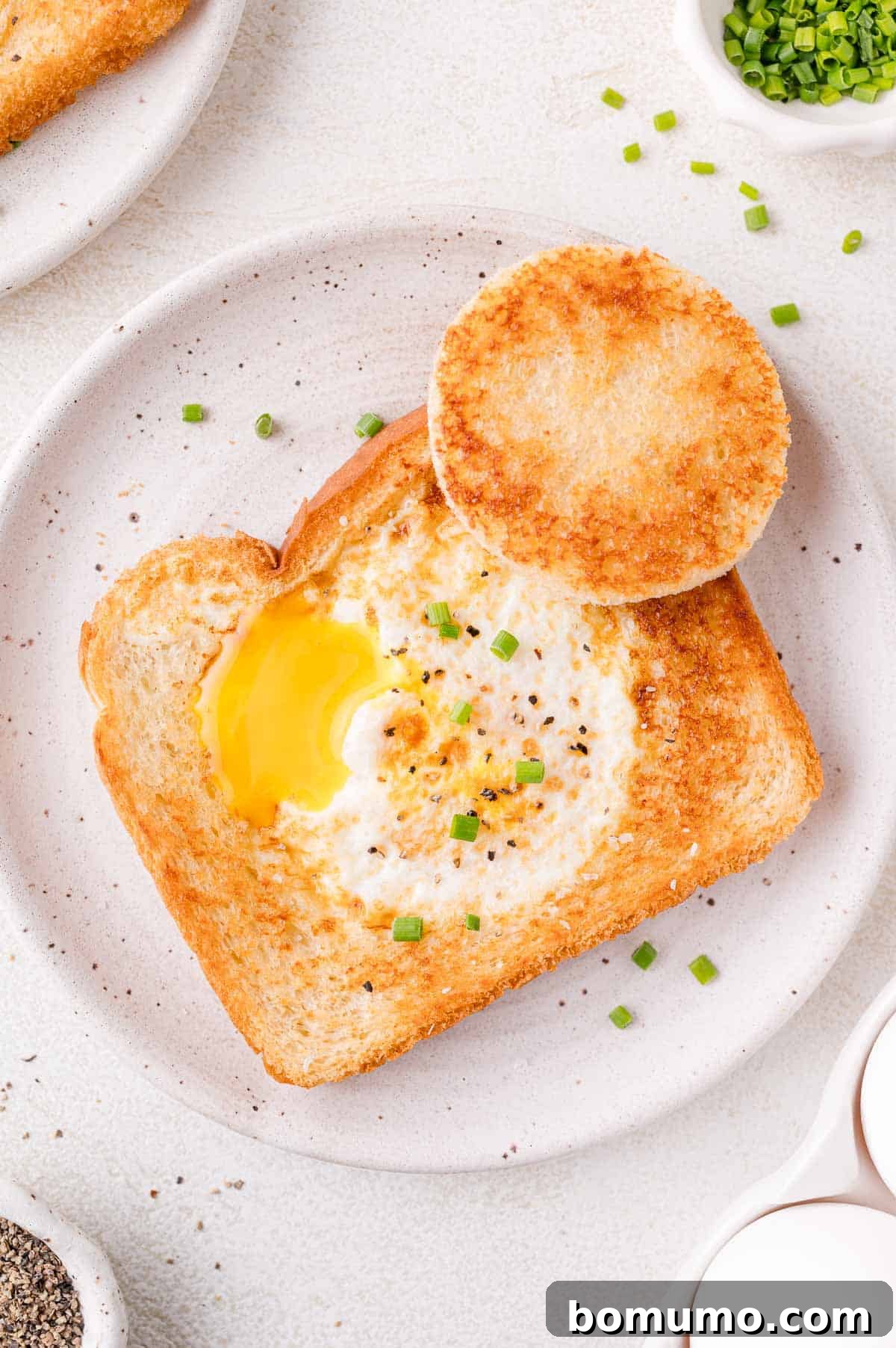 Egg in a basket garnished with chopped chives and served on a white plate.