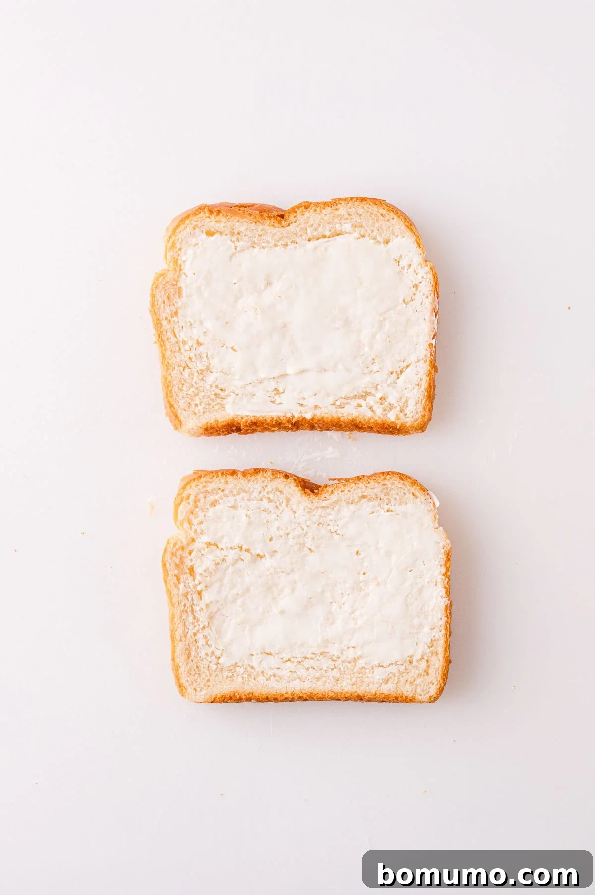 Two slices of bread with butter spread on top, placed on a white surface.