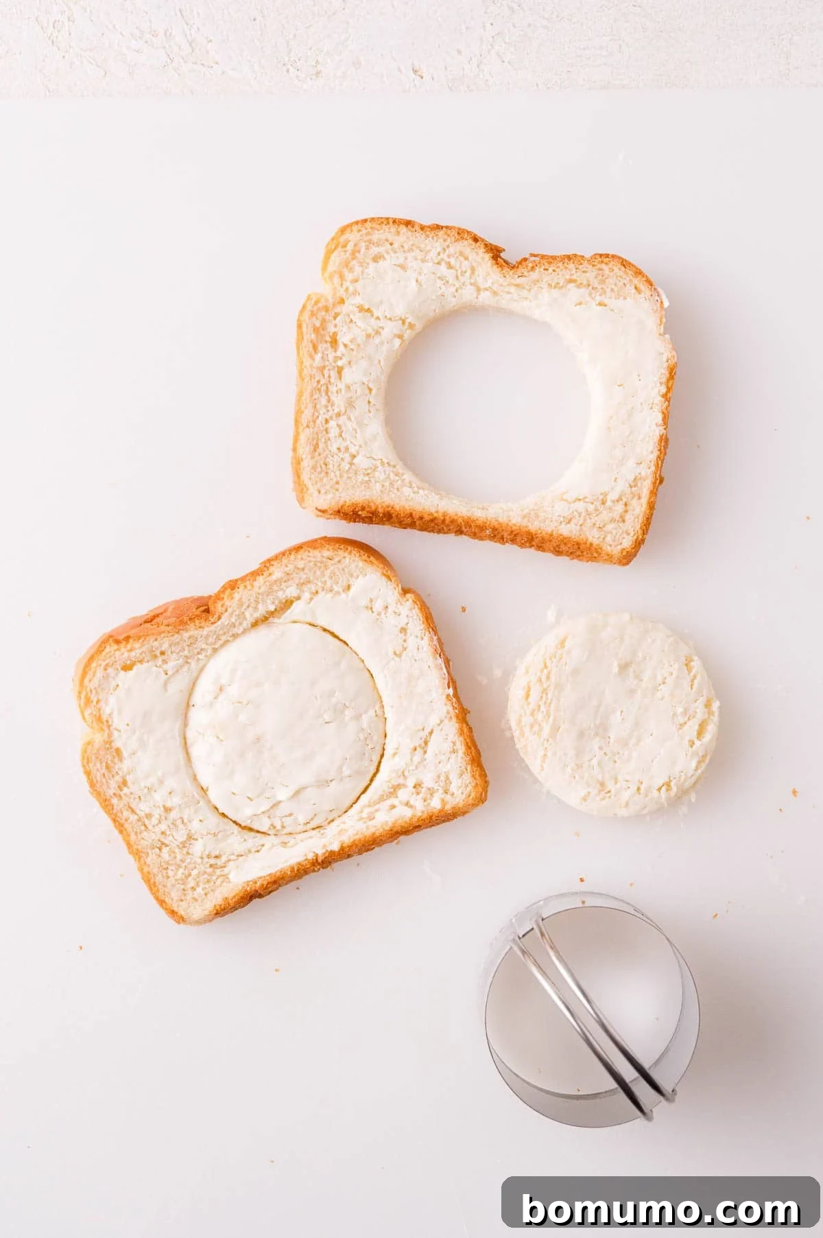 Two slices of bread with butter, one with a circular cutout, the other with a matching circular piece. A round cutter is nearby.