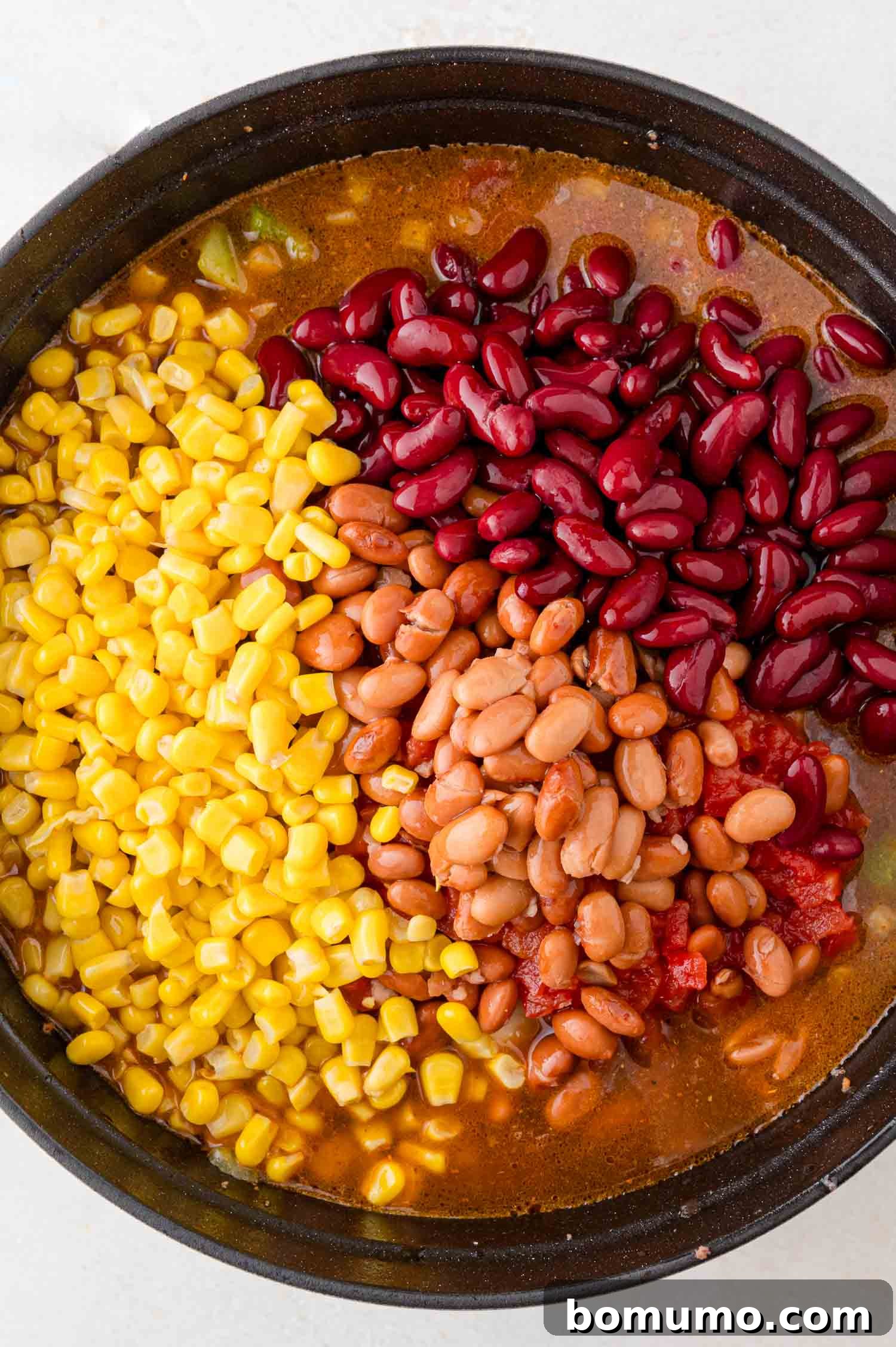 A hearty skillet featuring plump kidney beans, savory pinto beans, sweet corn, and vibrant diced tomatoes, all simmering together in a rich, flavorful sauce.