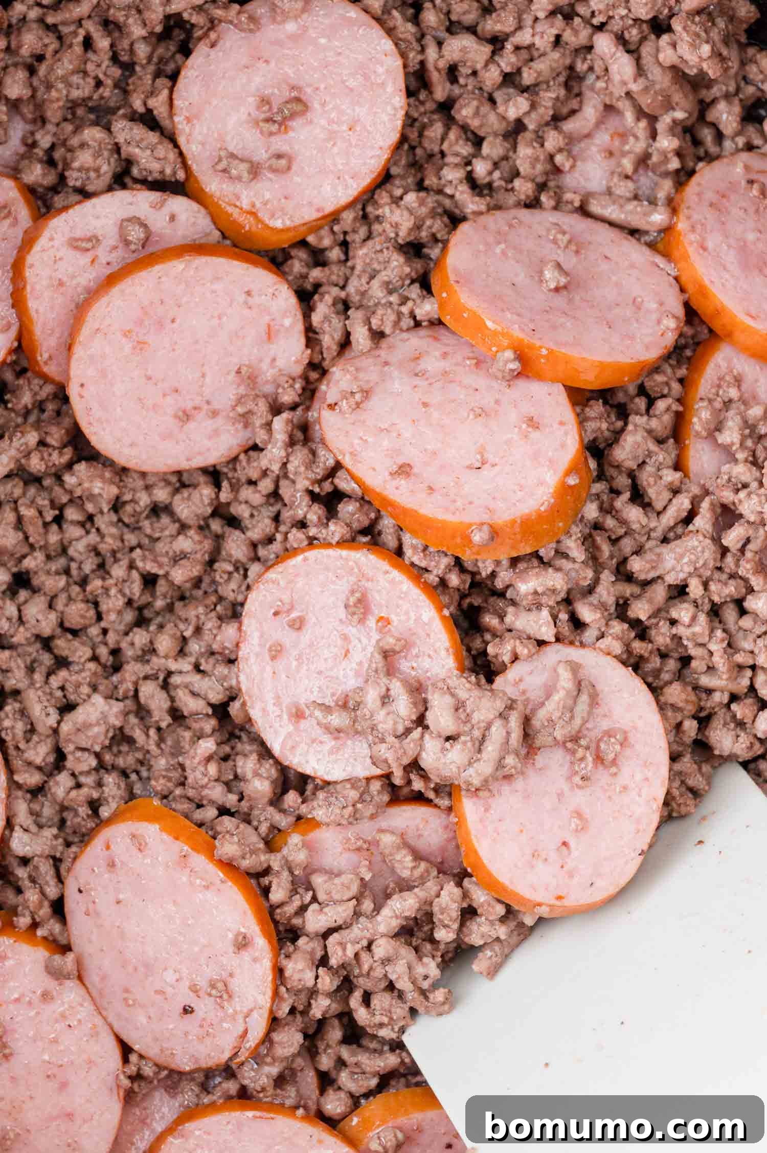 Sliced sausage rounds expertly mixed with savory cooked ground beef, creating a delicious base for the stew.