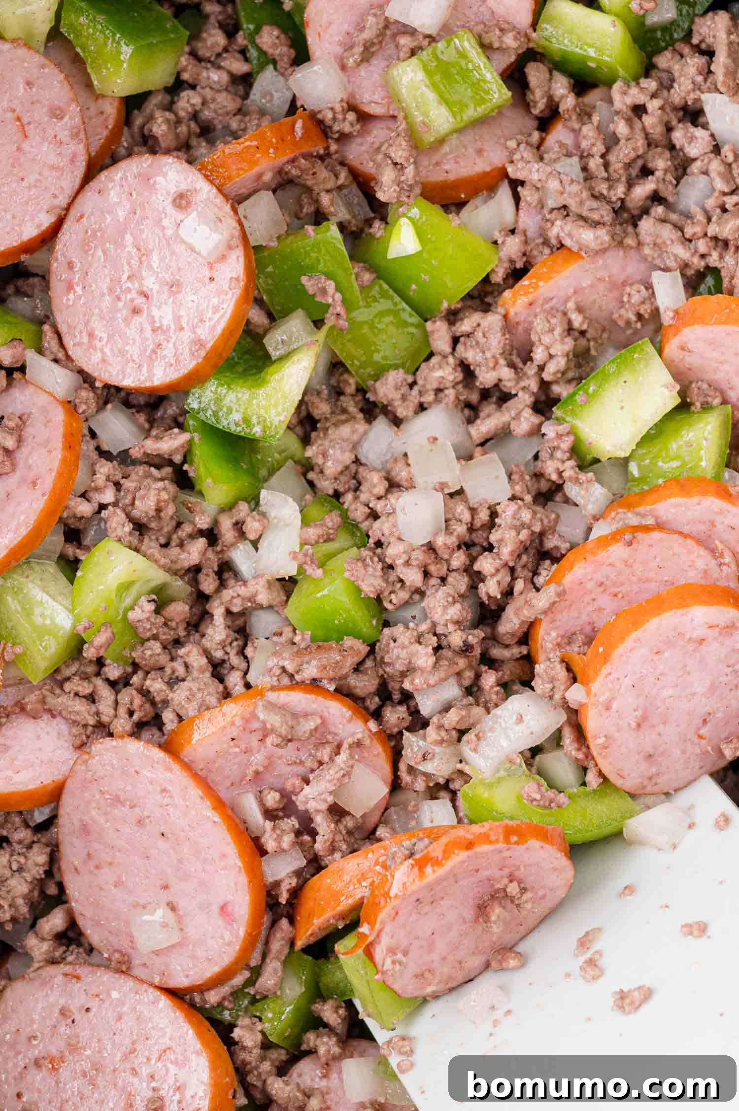 A delicious medley of chopped sausage, finely ground meat, vibrant green bell peppers, and diced onions, all mixed together in the pot.