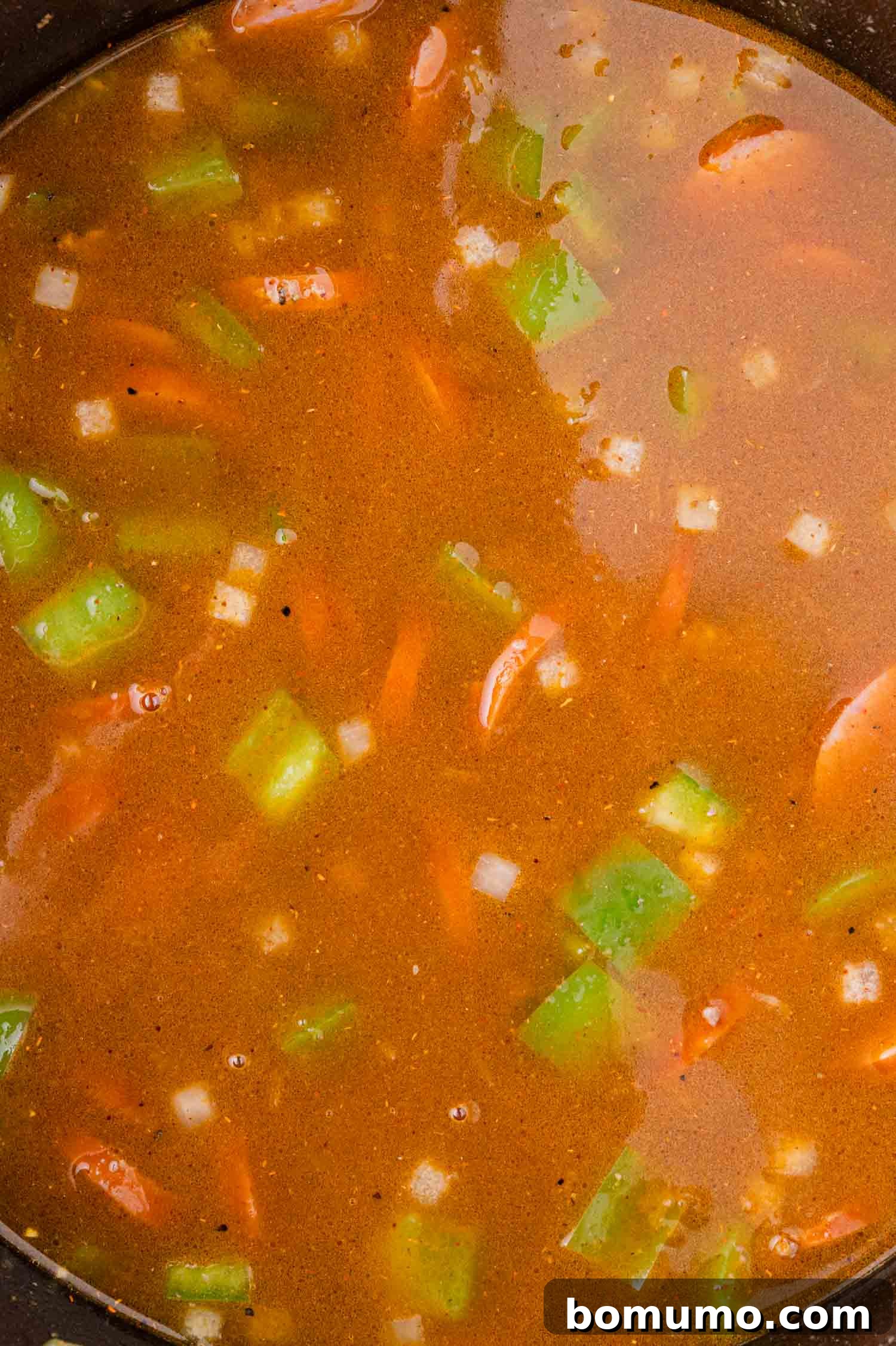 A robust pot of soup, featuring tender chopped green bell peppers, savory sliced sausage, and sweet diced onions, all simmering in a rich, brown broth.