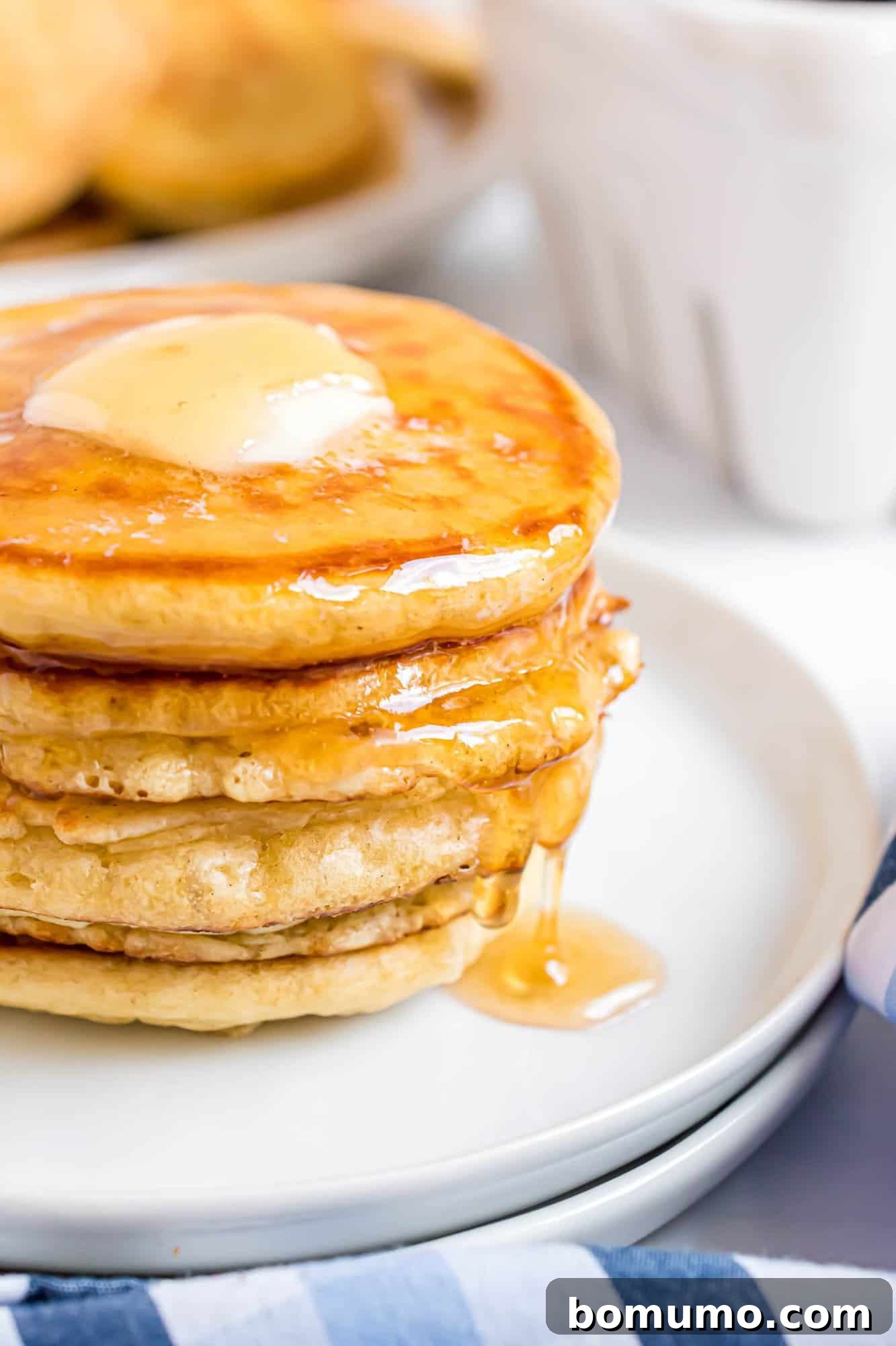 A stack of silver dollar pancakes with a pat of butter on top, drizzled with syrup, on a white plate.