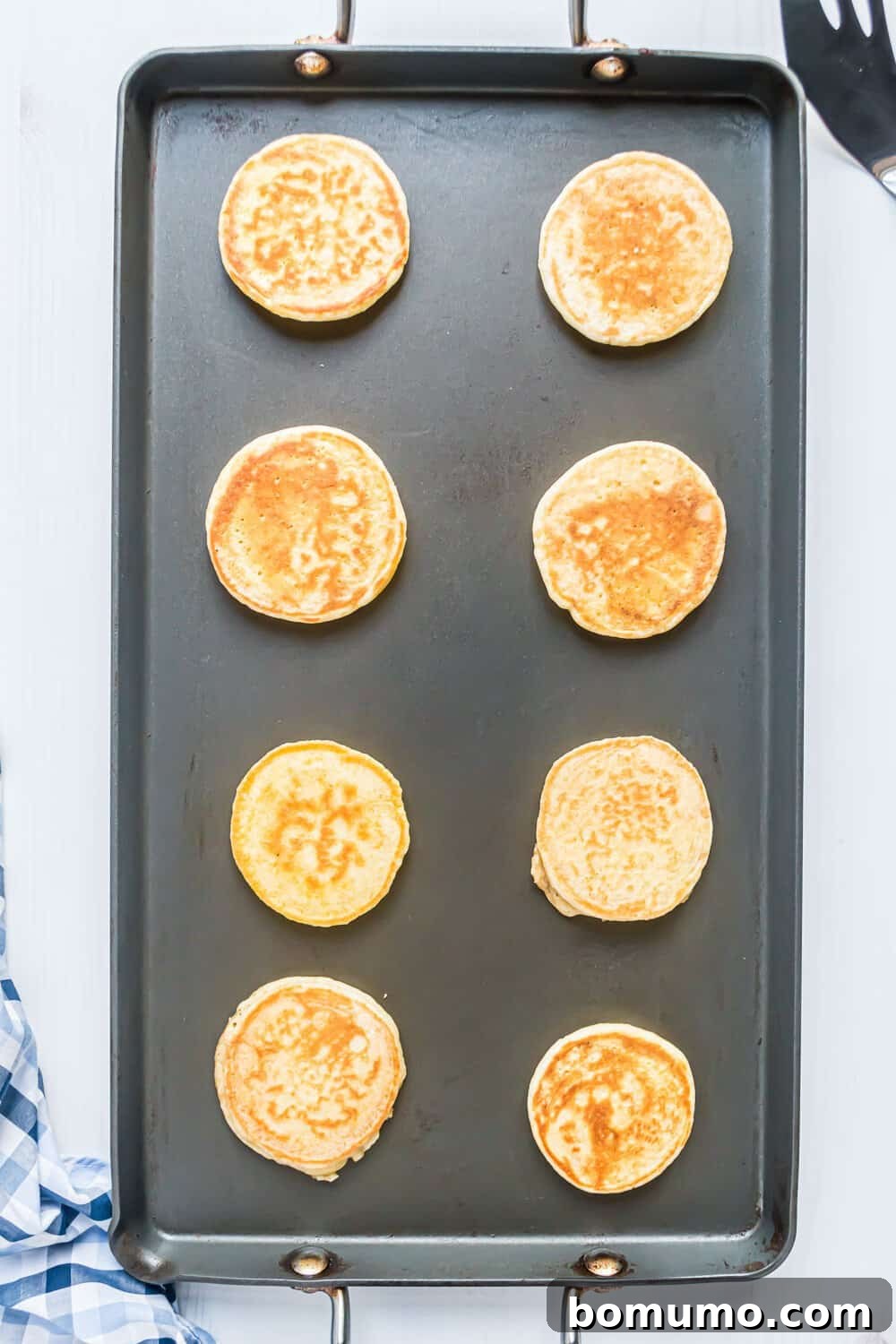 Eight golden brown pancakes cooking on a rectangular griddle.