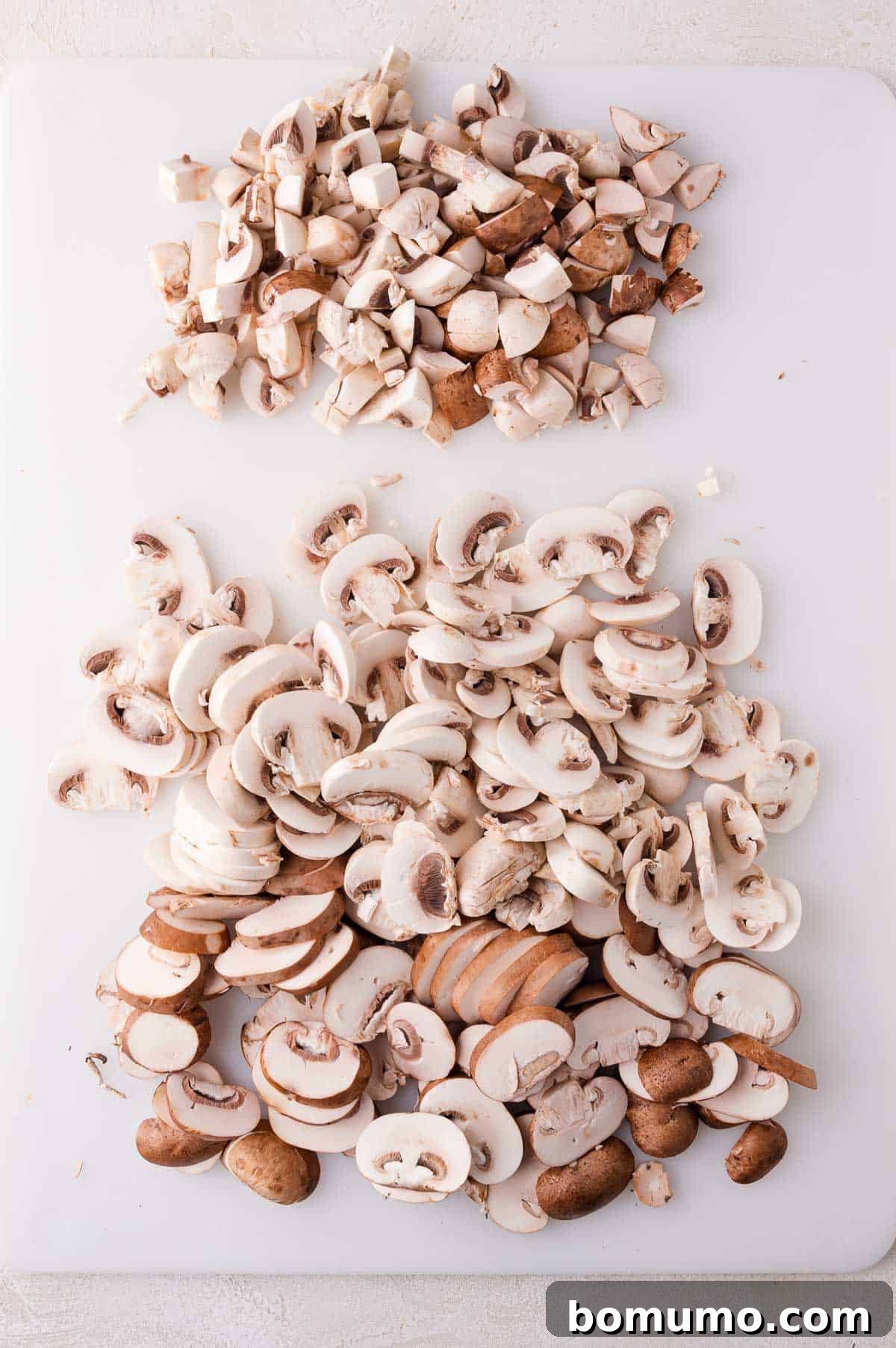 Chopped mushrooms on a white cutting board, with diced pieces at the top and sliced pieces below.