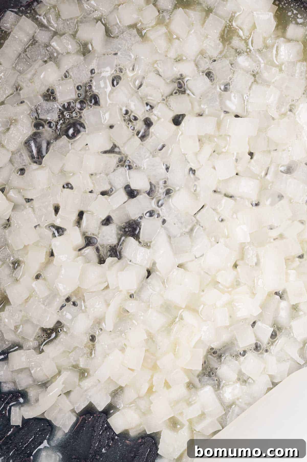 Diced onions being sautéed in oil in a pan.