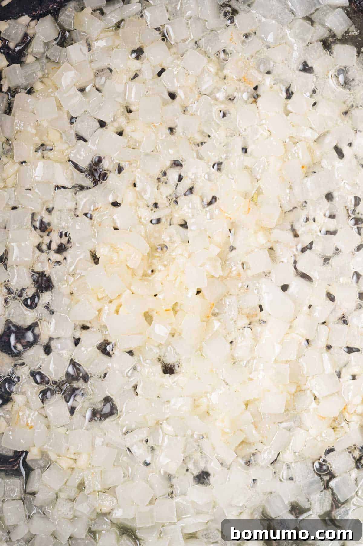 Close-up of translucent, diced onions, lightly coated in a clear, glossy liquid, with minced garlic on top.