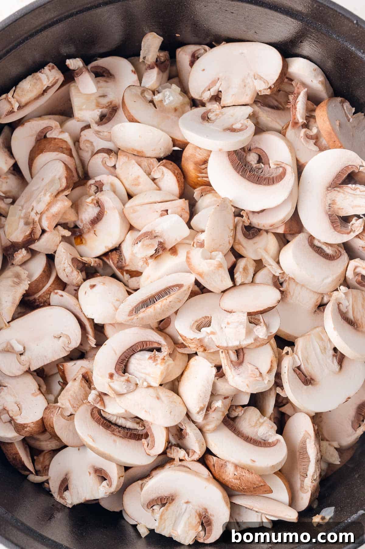 Sliced white mushrooms in a skillet, ready for cooking.