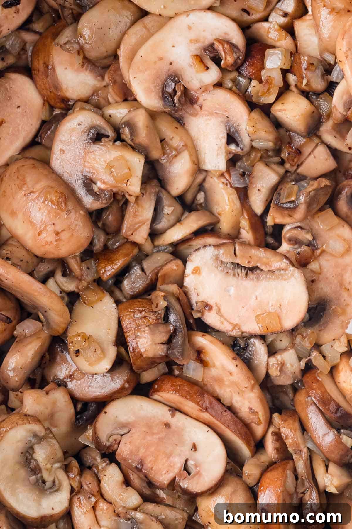 Sautéed mushrooms and onions in a pan, with sliced brown and white mushroom pieces evenly distributed.