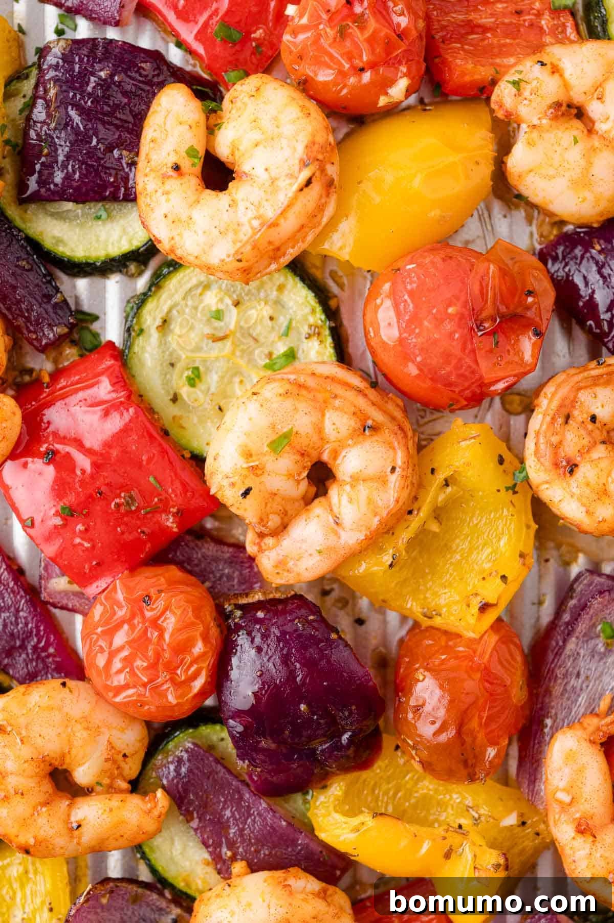 Shrimp, cherry tomatoes, red onion, bell peppers, and zucchini arranged on a baking sheet.