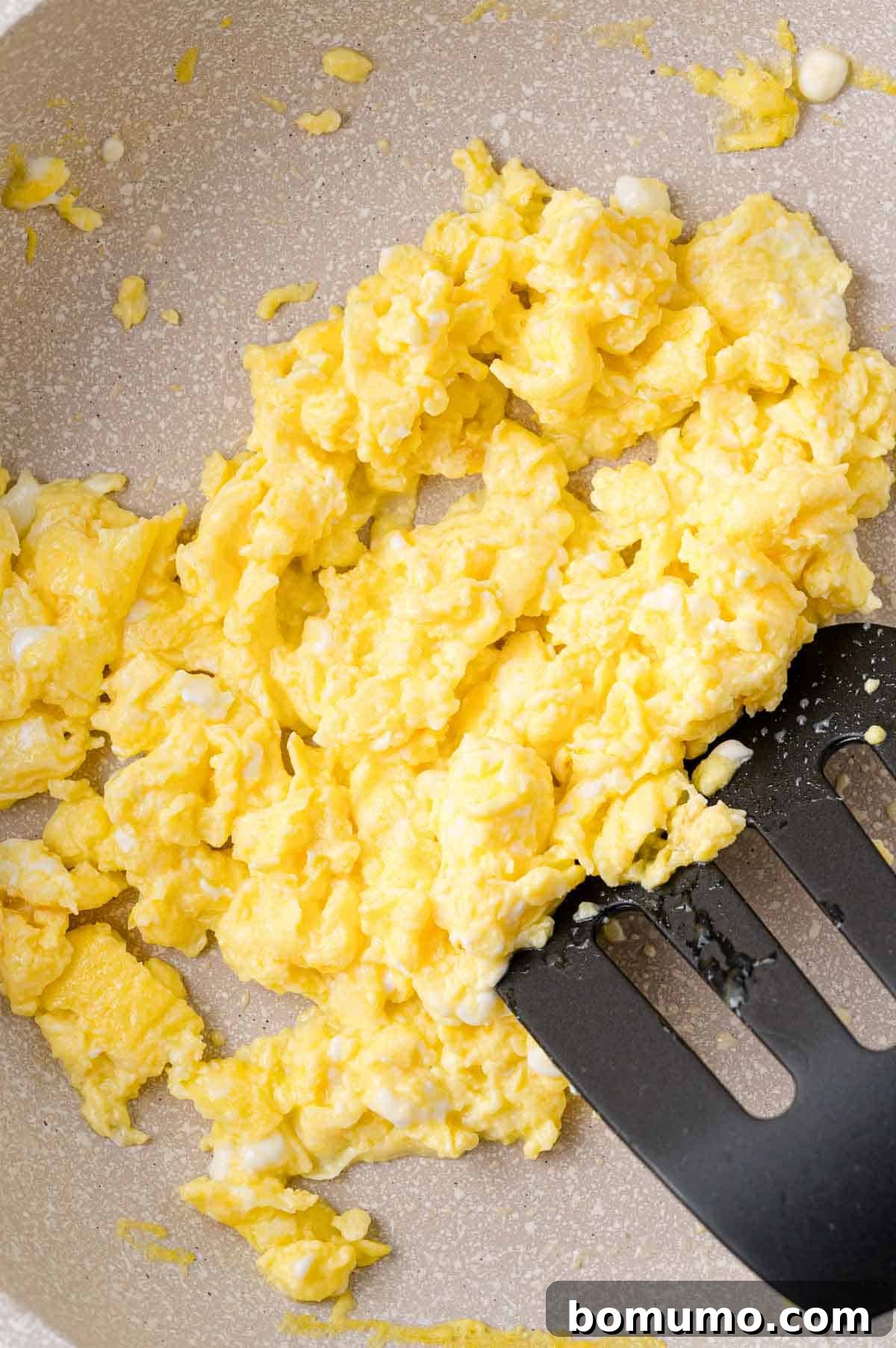 Scrambling eggs in a nonstick pan, with a black silicone spatula gently moving the curds as they cook to a perfect, fluffy consistency.