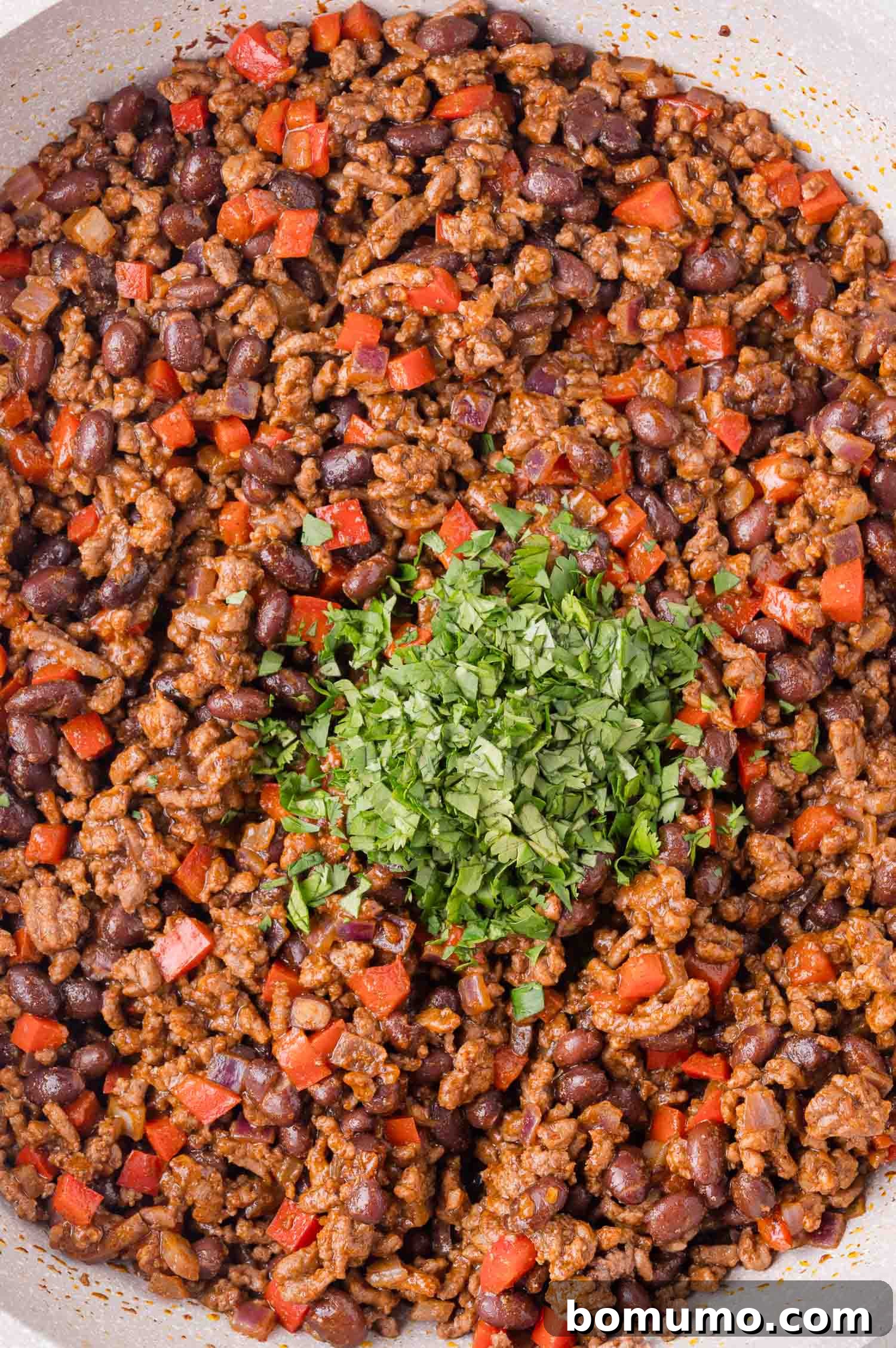 Effortless Sheet Pan Quesadillas 9 A cooked mixture of ground beef, black beans, and diced red peppers, topped with a garnish of chopped fresh cilantro in the center, adding a fresh finish.