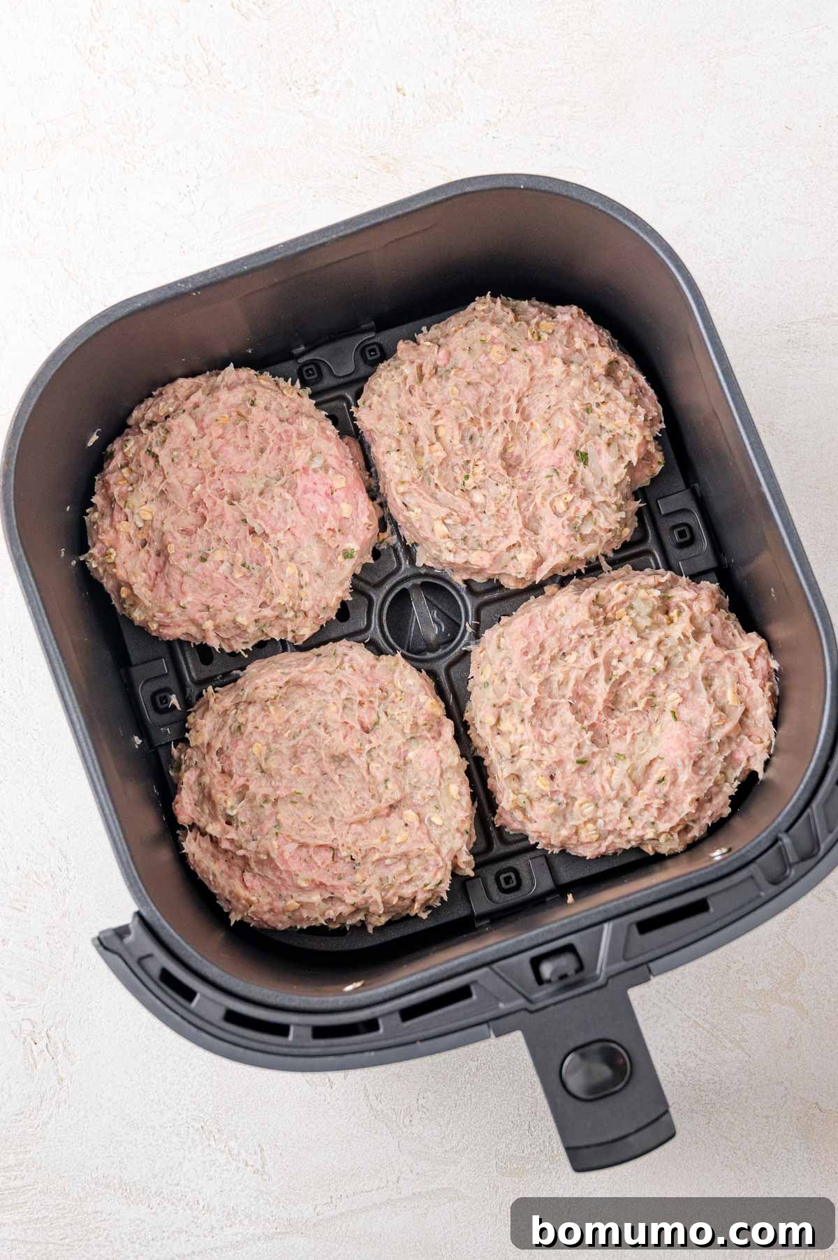 Four raw, perfectly formed turkey burger patties are carefully placed inside the basket of an air fryer, awaiting their transformation.