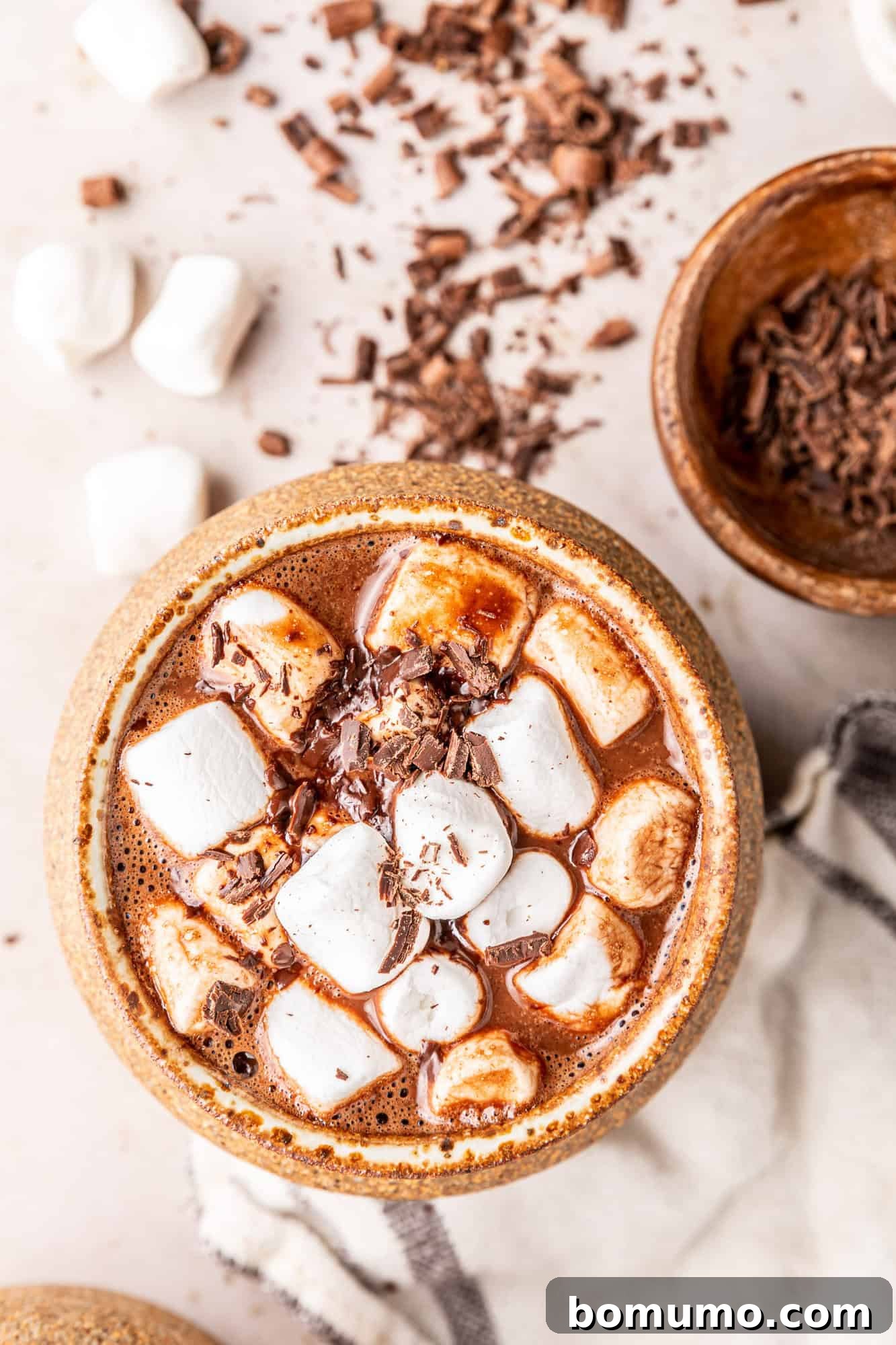 Overhead view of oat milk hot chocolate topped with marshmallows in an earth-toned mug, highlighting its creamy texture.