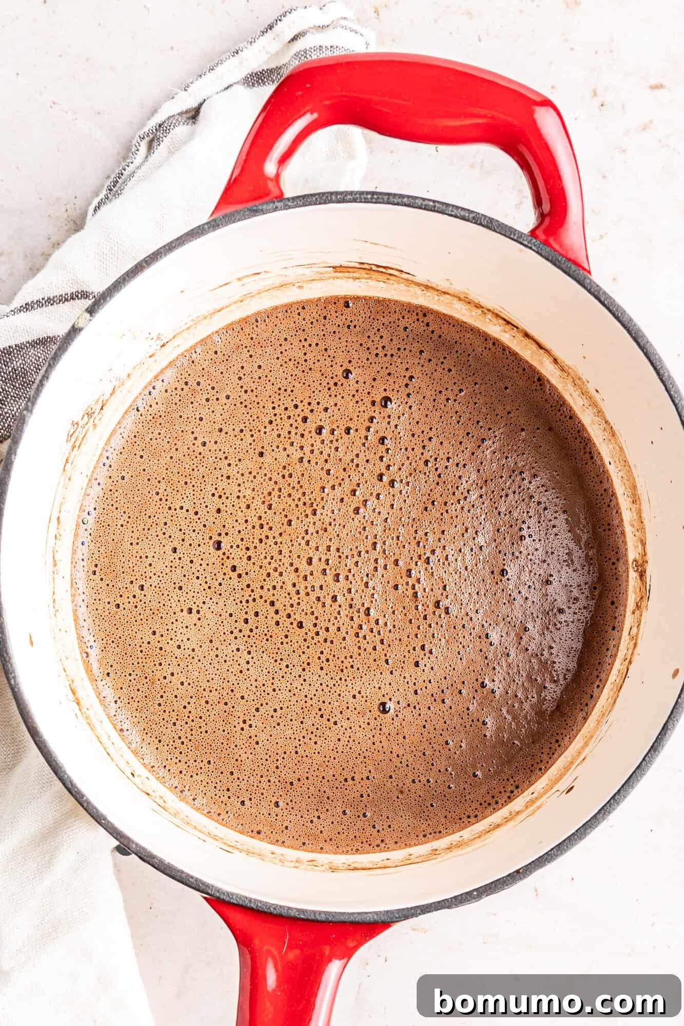 Oat milk hot chocolate gently simmering in a small red saucepan, showcasing its smooth, rich consistency.