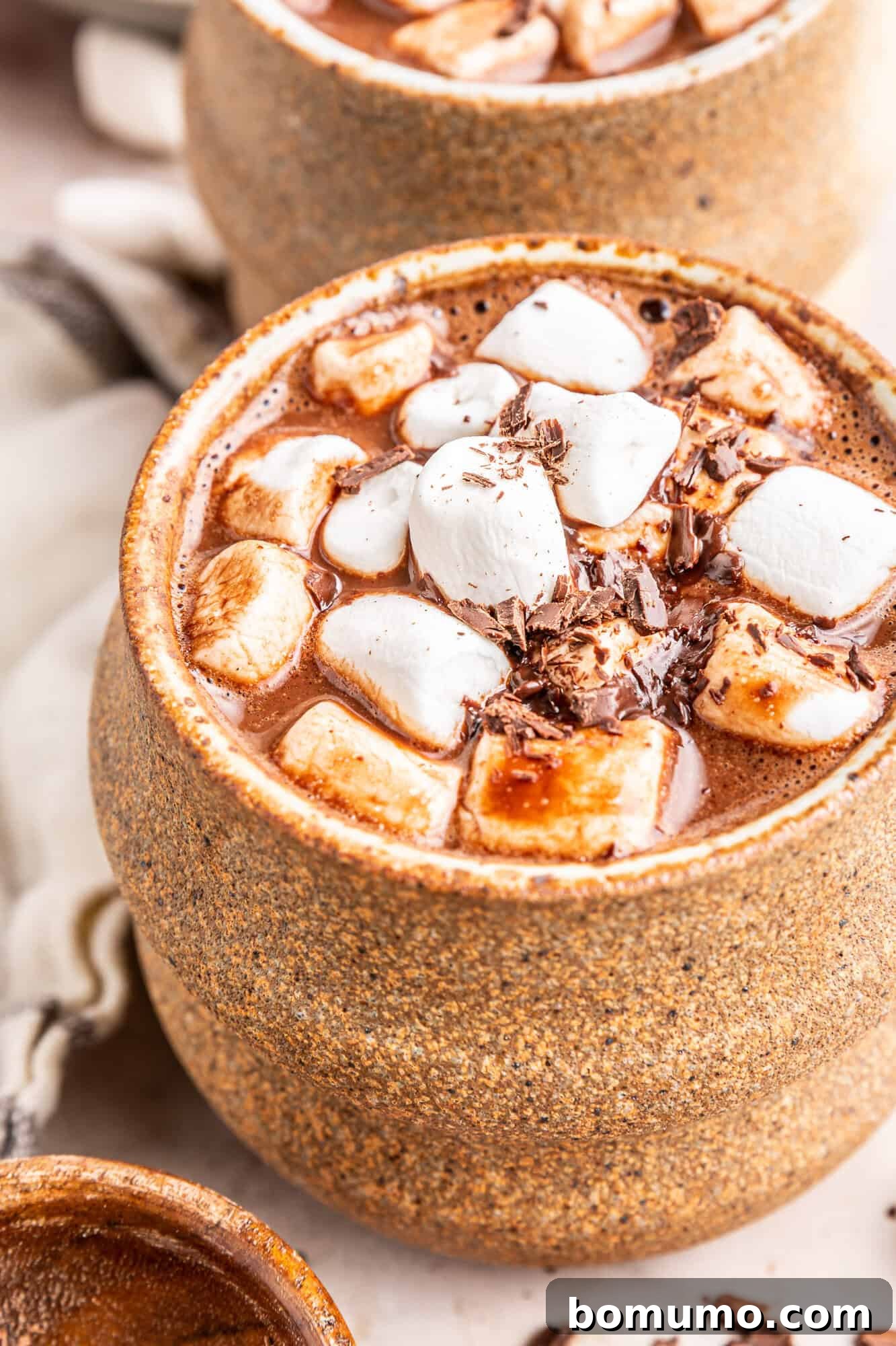 An inviting earth-toned mug filled with creamy oat milk hot chocolate, generously topped with fluffy mini-marshmallows.