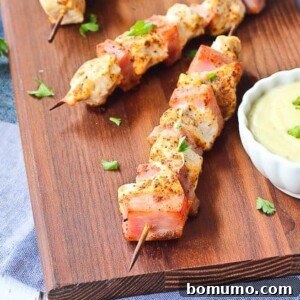 Partial overhead of golden-brown chicken and ham kabobs with a side of creamy Swiss cheese dipping sauce.