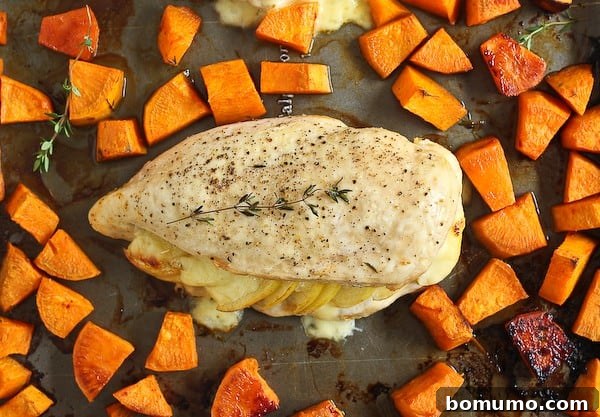 An overhead view of a single stuffed chicken breast and roasted sweet potatoes on a sheet pan, showcasing the vibrant colors and textures.