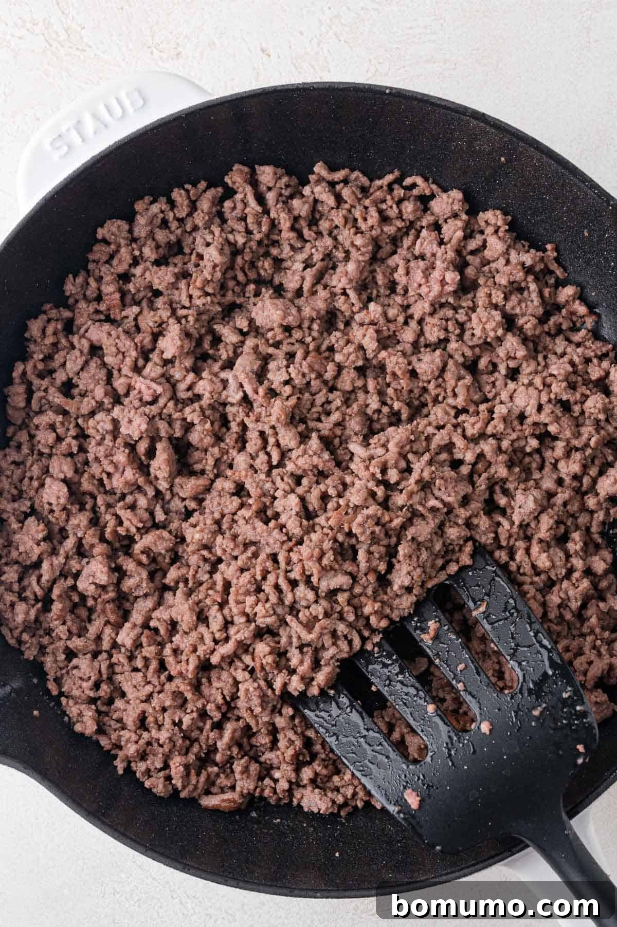 Classic Cheeseburger Salad 4 Close-up of perfectly cooked, crumbled ground beef, seasoned and browned, resting in a black skillet with a black spatula, ready to be incorporated into the salad.