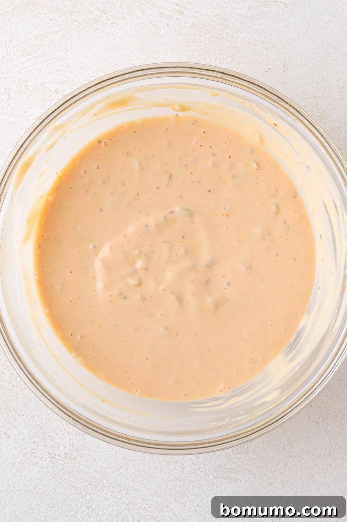 Classic Cheeseburger Salad 6 A smooth, creamy, orange-beige Big Mac sauce, perfectly blended, fills a glass bowl on a pristine white surface, ready to be drizzled over the salad.