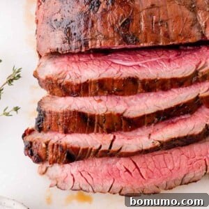 Sliced medium-rare grilled flank steak on a white surface, showing a pink center and seared outer edges. A sprig of thyme is visible to the side.