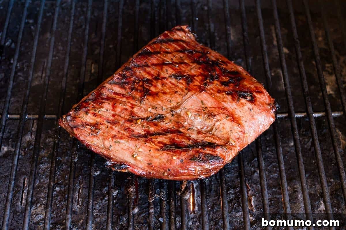 A grilled steak with grill marks sits on a metal barbecue grate.