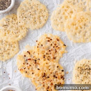 Several round parmesan crisps with spices, such as black pepper and red pepper flakes, are arranged on crinkled white parchment paper, showcasing their appetizing appearance.