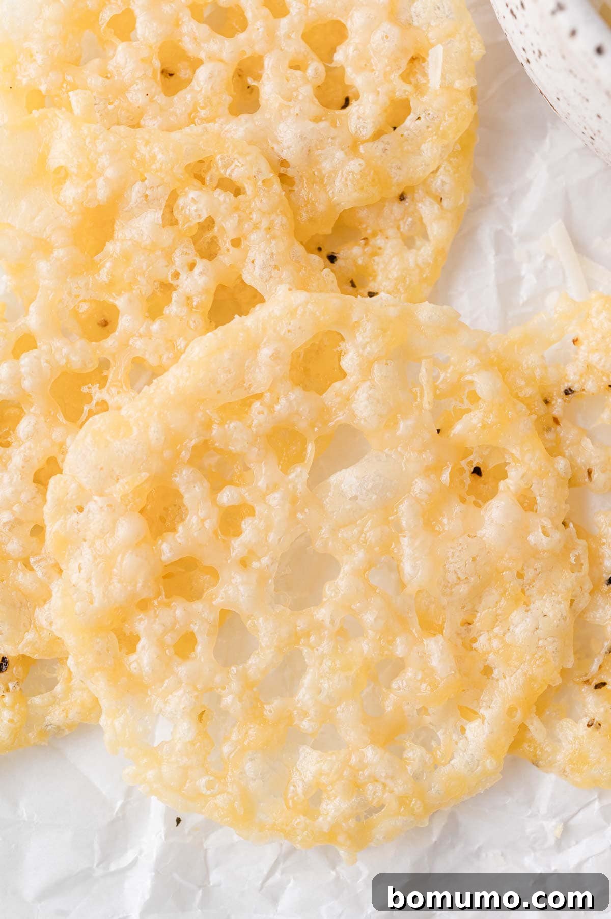 Close-up of several perfectly round, golden, and lacy Parmesan crisps resting on a sheet of white parchment paper, highlighting their delicate, airy texture.