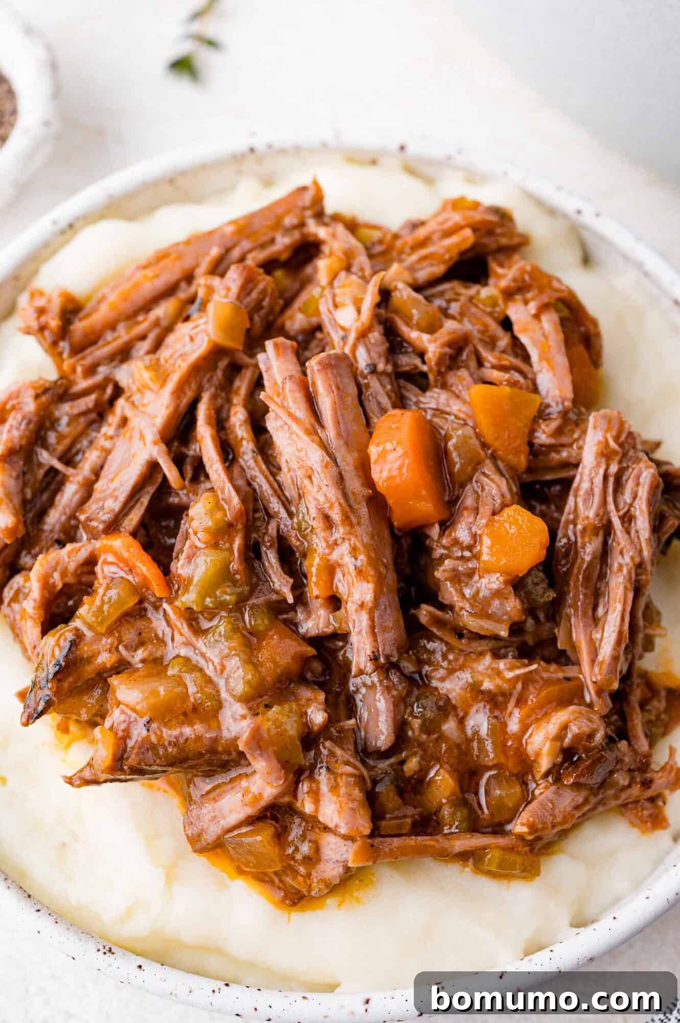 A plate of shredded braised beef with carrots and gravy on a bed of mashed potatoes.