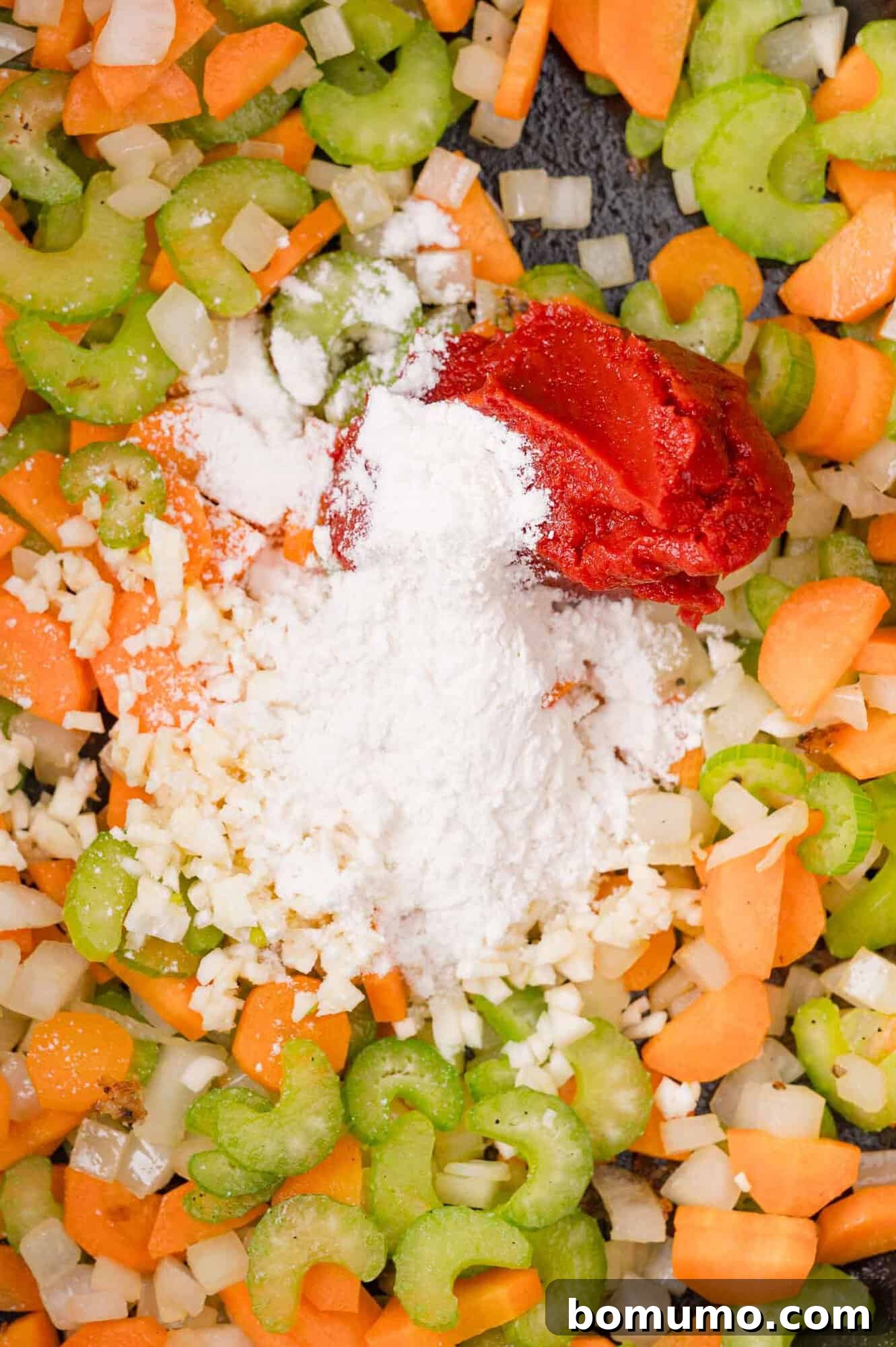 Chopped carrots, celery, and onions with a pile of flour and a dollop of tomato paste on top.