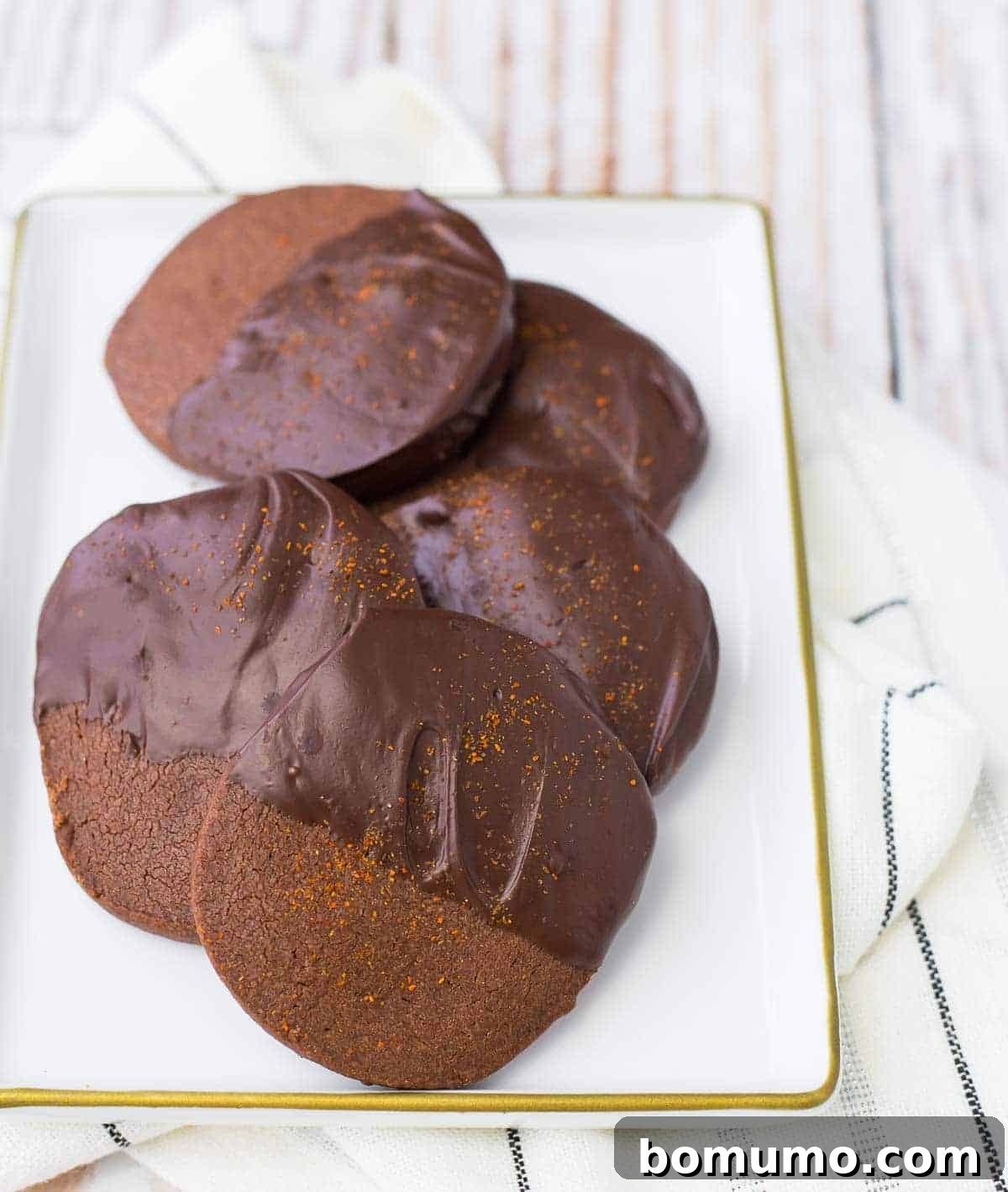 Aztec Chocolate Shortbread Delights 2 A collection of beautifully crafted Mexican Chocolate Shortbread Cookies arranged on a pristine white square plate, set against a light background, highlighting their rich chocolate hue and delicate dusting.