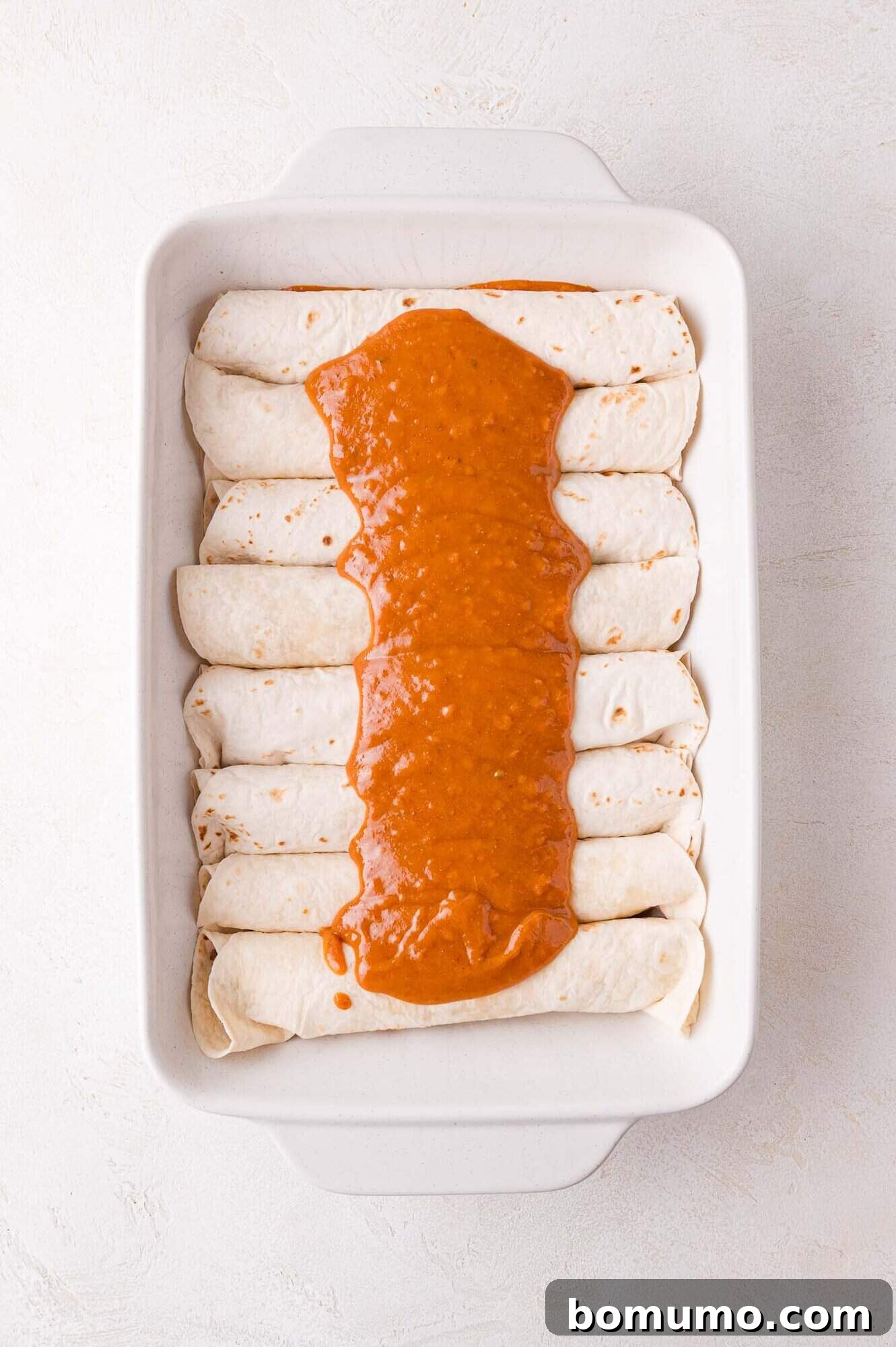 Hearty Beef Enchilada Bake 11 A baking dish with evenly arranged rolled tortillas topped with a thick layer of red sauce down the middle.