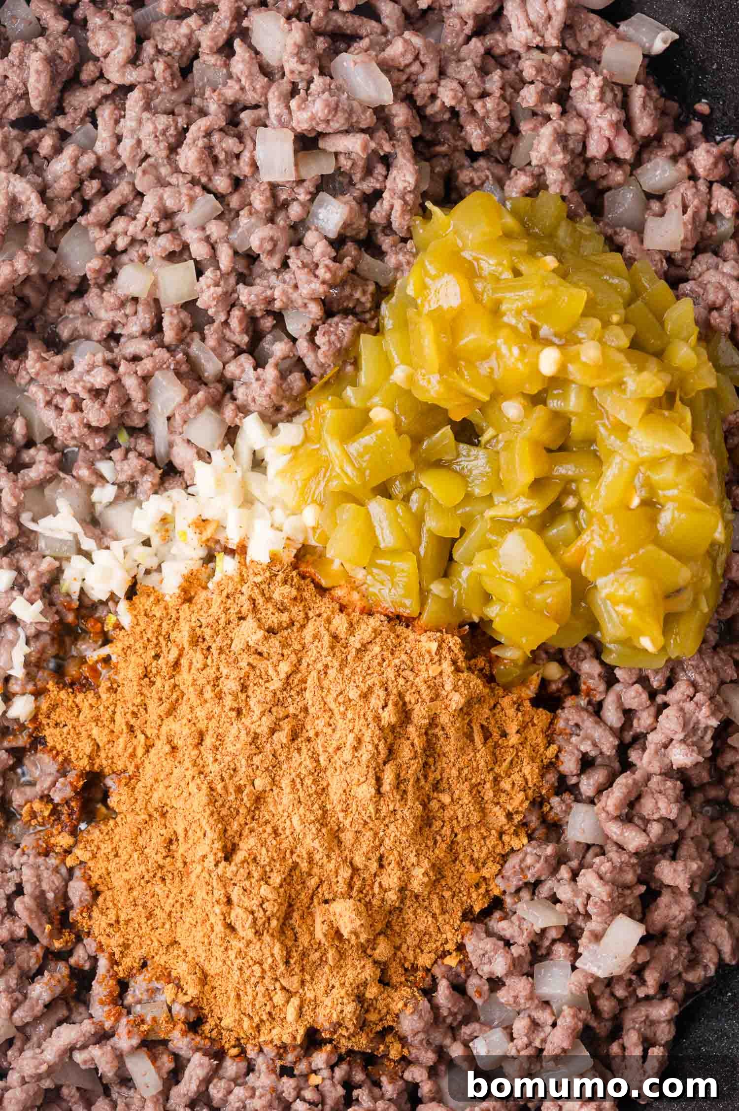Hearty Beef Enchilada Bake 6 Ground beef in a pan with chopped onions, taco seasoning, minced garlic, and chopped green chiles on top, ready to be mixed.