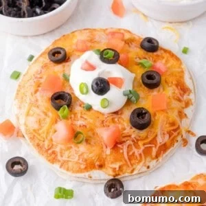 Mexican pizza topped with melted cheese, diced tomatoes, black olives, green onions, and a dollop of sour cream.