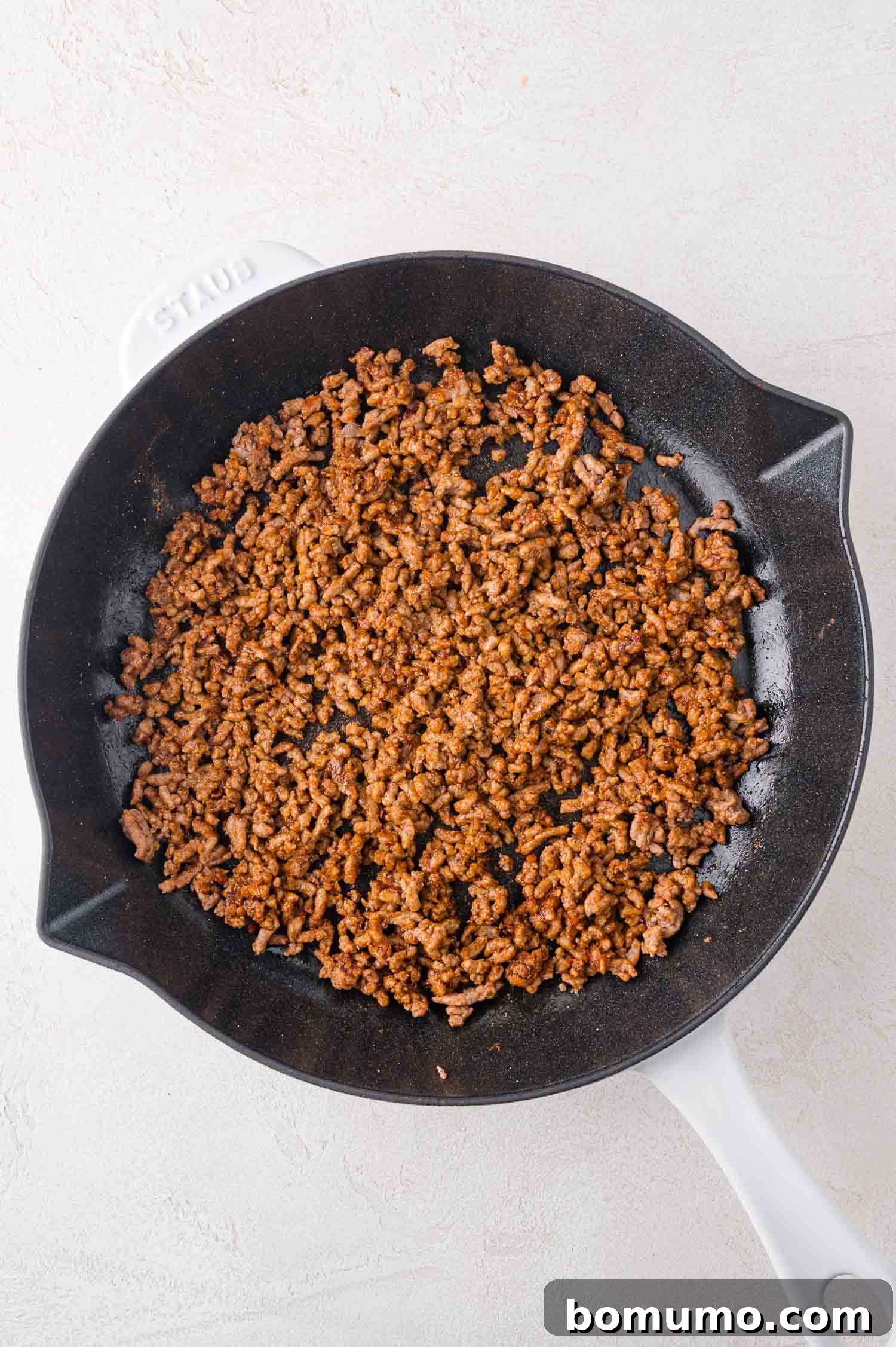 A sturdy black skillet containing perfectly browned ground beef, resting on a clean, light-colored countertop, ready for seasoning.