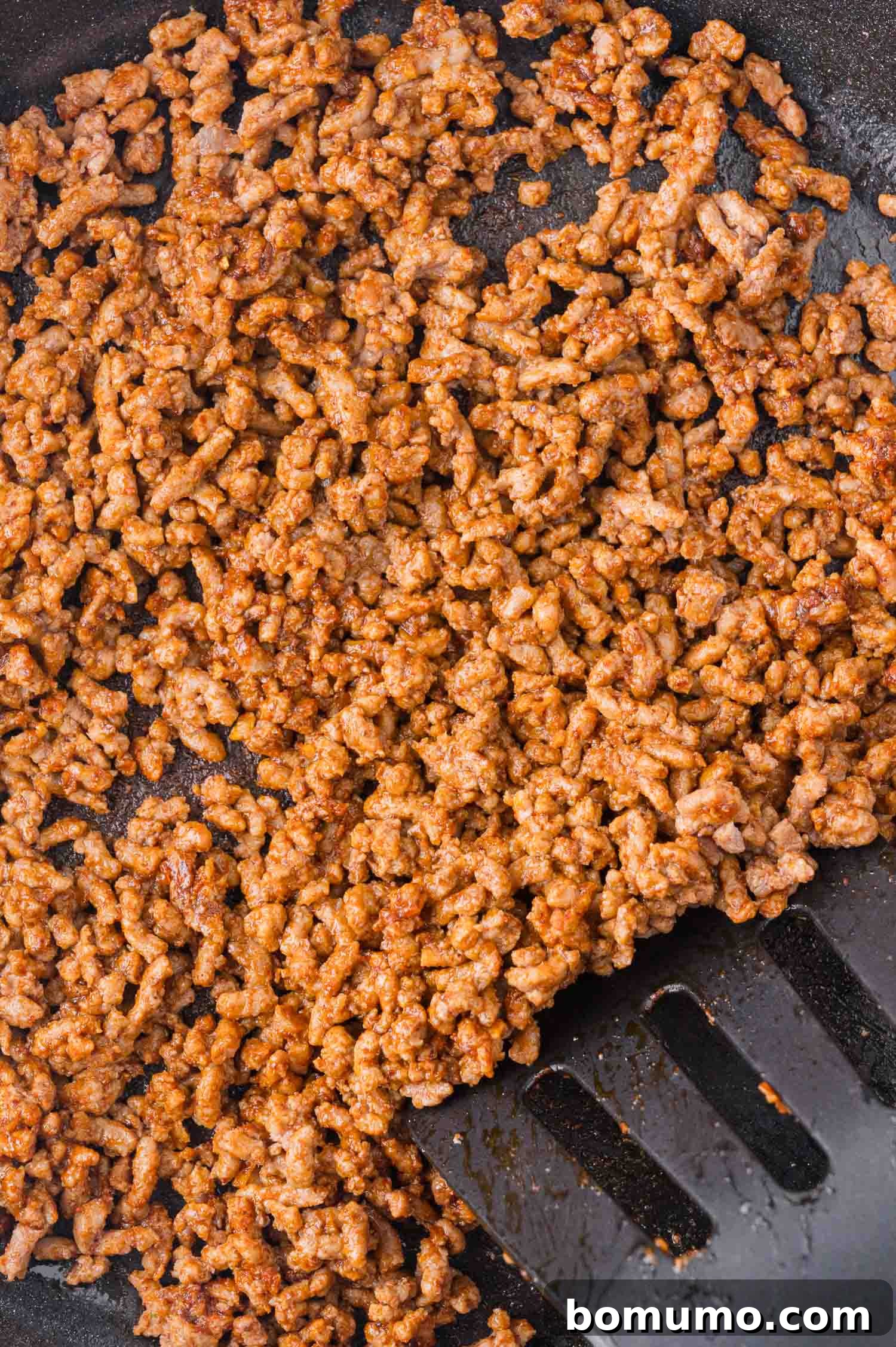 Spiced ground beef sizzling and cooking in a skillet, being skillfully broken apart and evenly spread with a spatula, achieving a perfect brown.