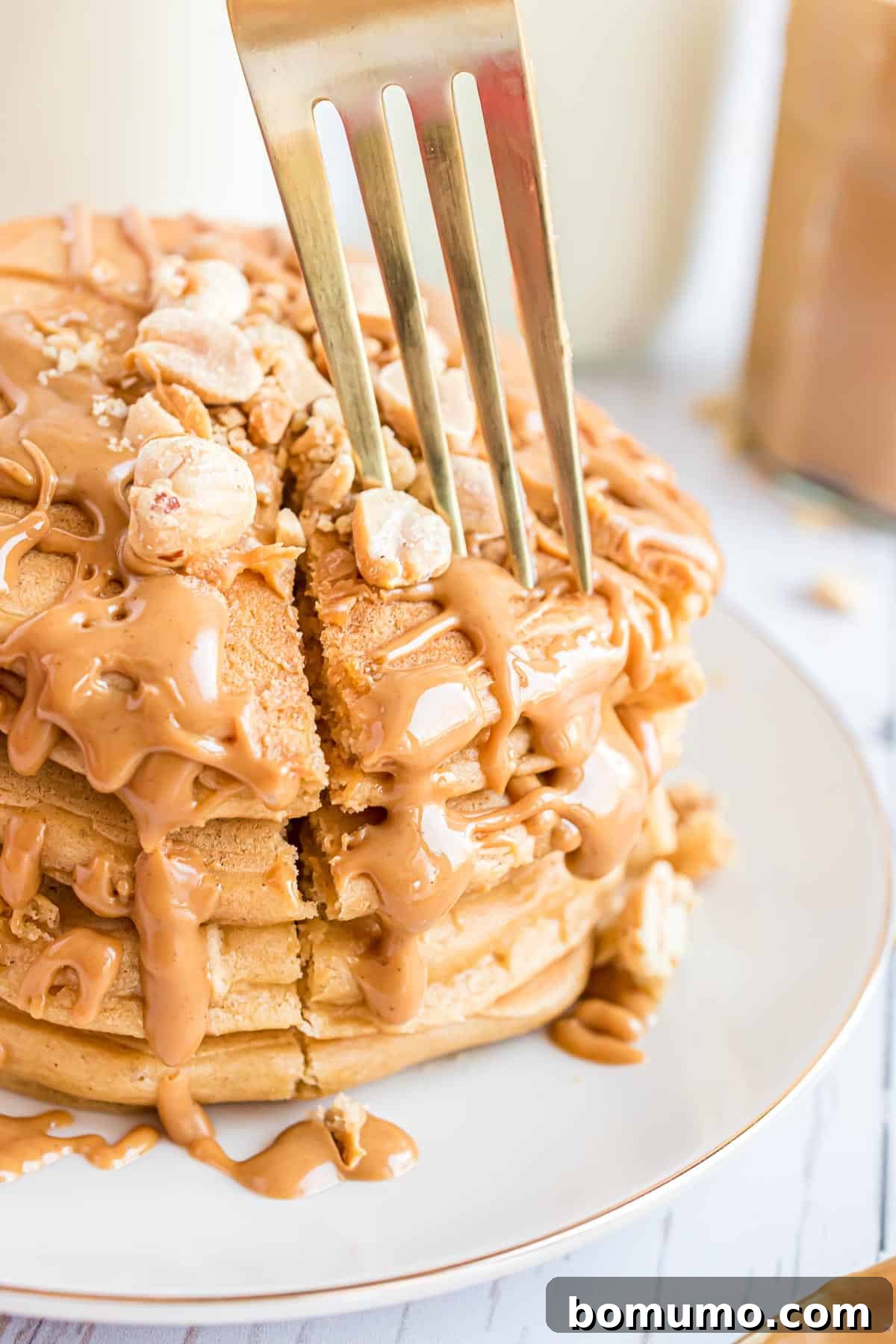 A inviting stack of golden-brown peanut butter pancakes, lavishly coated with a rich peanut butter syrup and adorned with a scattering of finely chopped nuts, promising a delightful texture with every mouthful.