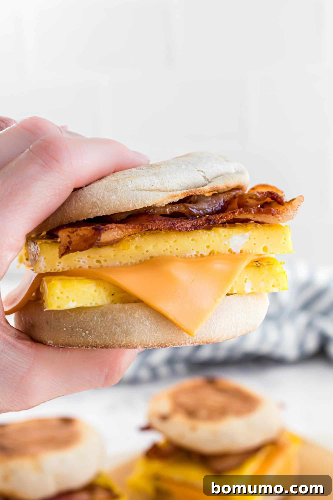 Breakfast Sandwich Bliss 2 Hand holding a breakfast sandwich with egg, melted cheese, and bacon between English muffin halves.