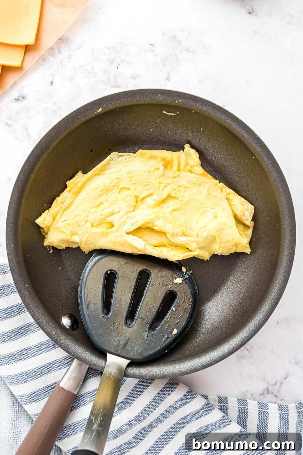 Breakfast Sandwich Bliss 16 Cooked scrambled eggs in a nonstick frying pan with a slotted spatula on a striped dish towel.