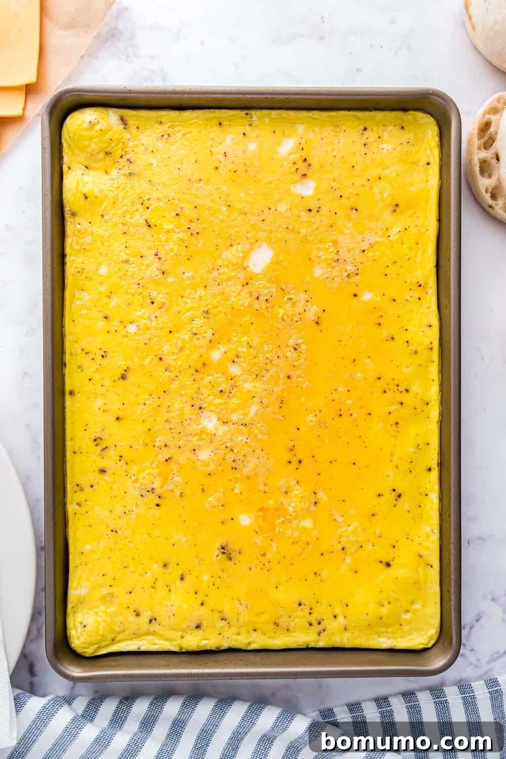 Breakfast Sandwich Bliss 9 Baked eggs in a rectangular pan, seasoned with visible salt and pepper. A striped cloth and pieces of bread are partially visible on the sides.