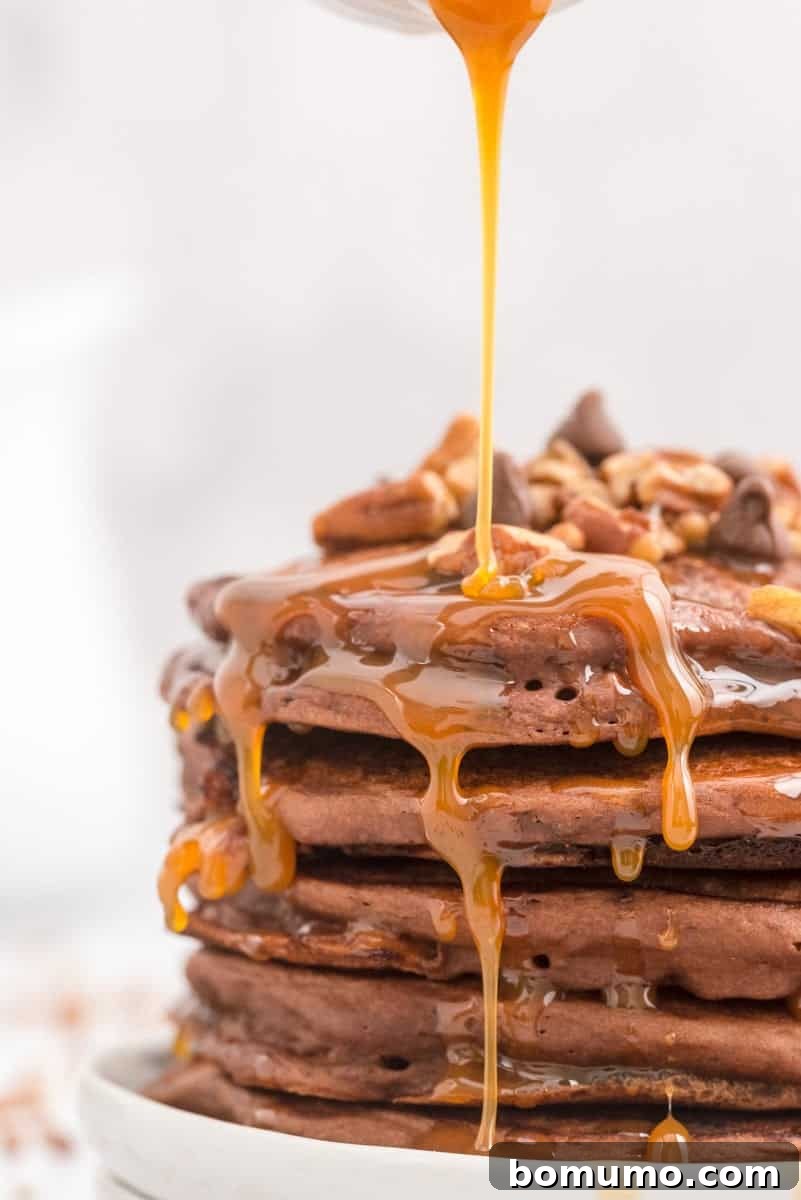 A stack of golden brown turtle pancakes with pecans and chocolate chips is generously topped with warm, dripping caramel sauce.