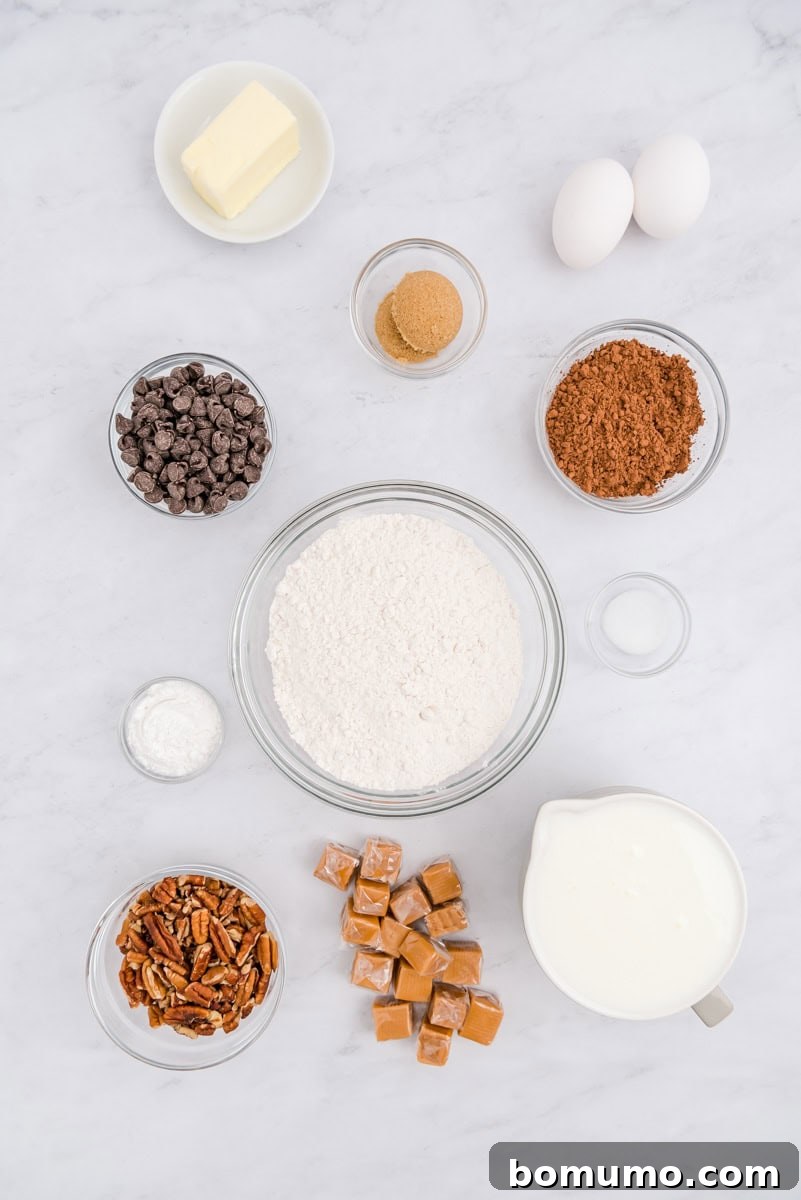A beautifully arranged collection of fresh ingredients on a white marble surface, including blocks of butter, whole eggs, rich brown sugar, unsweetened cocoa powder, an abundance of chocolate chips, baking powder, all-purpose flour, plump pecans, soft caramel squares, a sprinkle of salt, and a pitcher of creamy buttermilk.